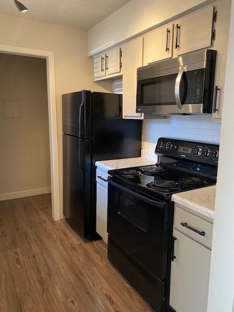 A kitchen with a black refrigerator , black stove , and stainless steel microwave.