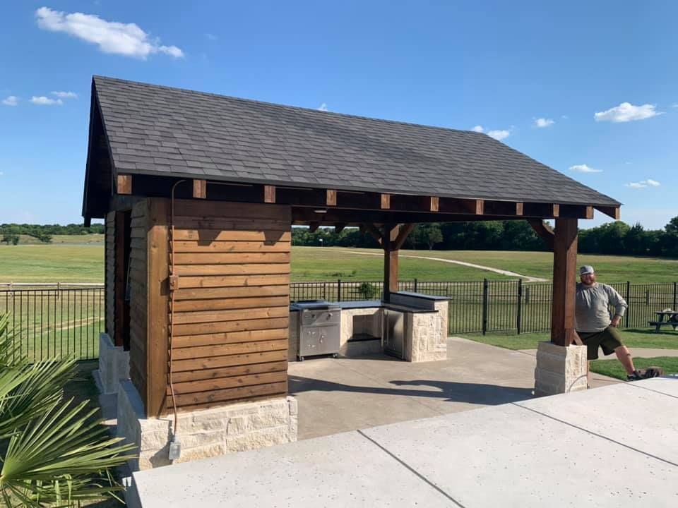 A man is standing in front of a wooden pavilion.