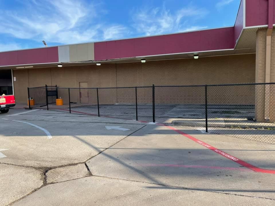 A red truck is parked in front of a building with a chain link fence.