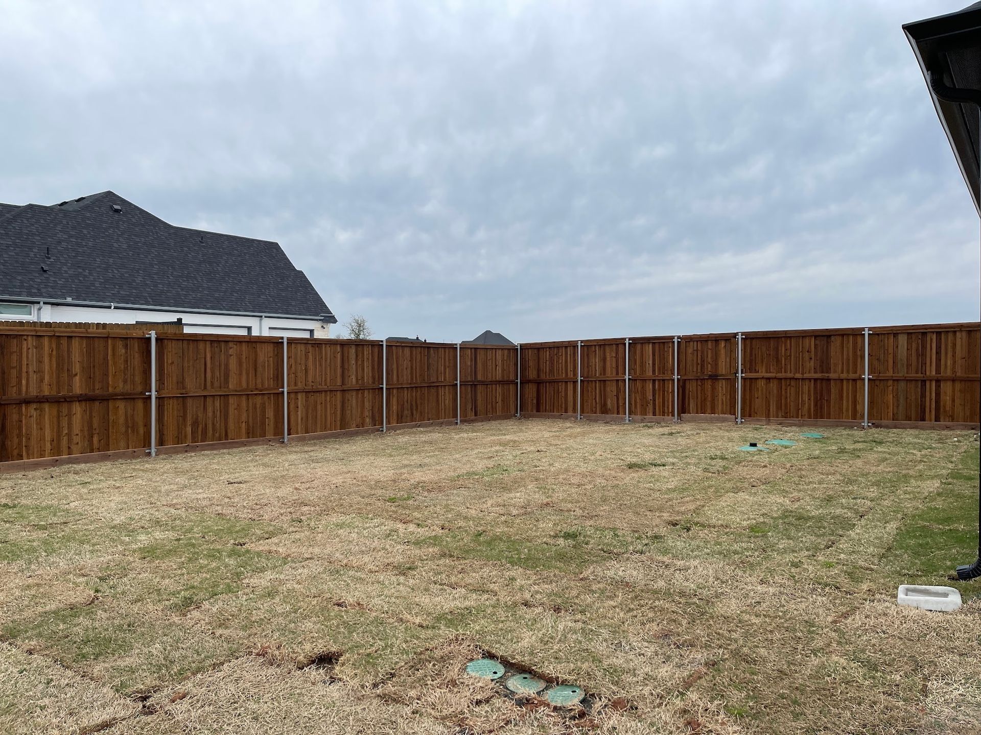 A backyard with a wooden fence and a house in the background.