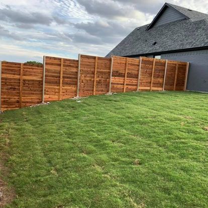 A wooden fence surrounds a lush green lawn in front of a house.