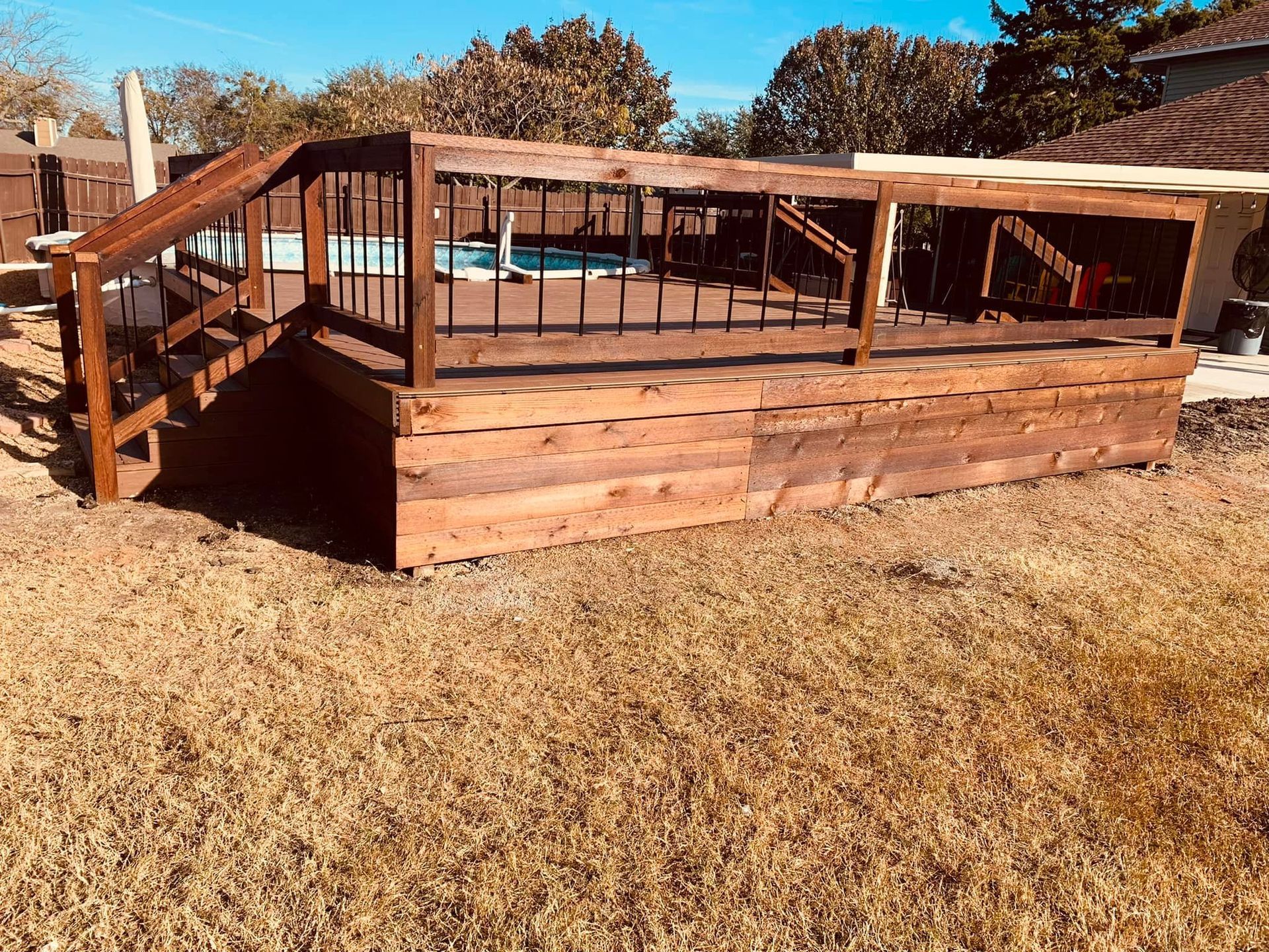 A wooden deck with stairs leading up to it and a pool in the background.