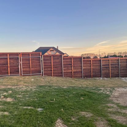 A wooden fence surrounds a grassy field with a house in the background.
