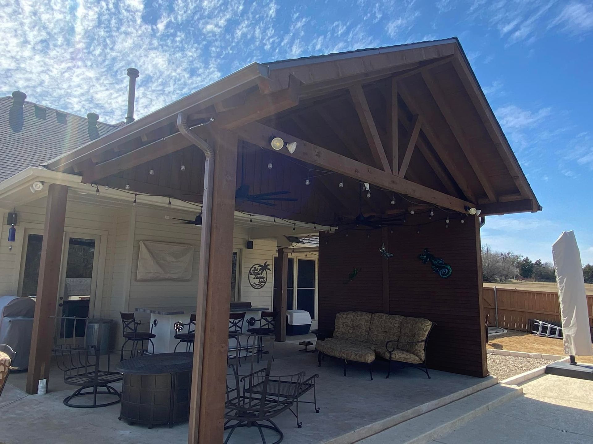A large covered patio area with a couch and chairs under a wooden roof.