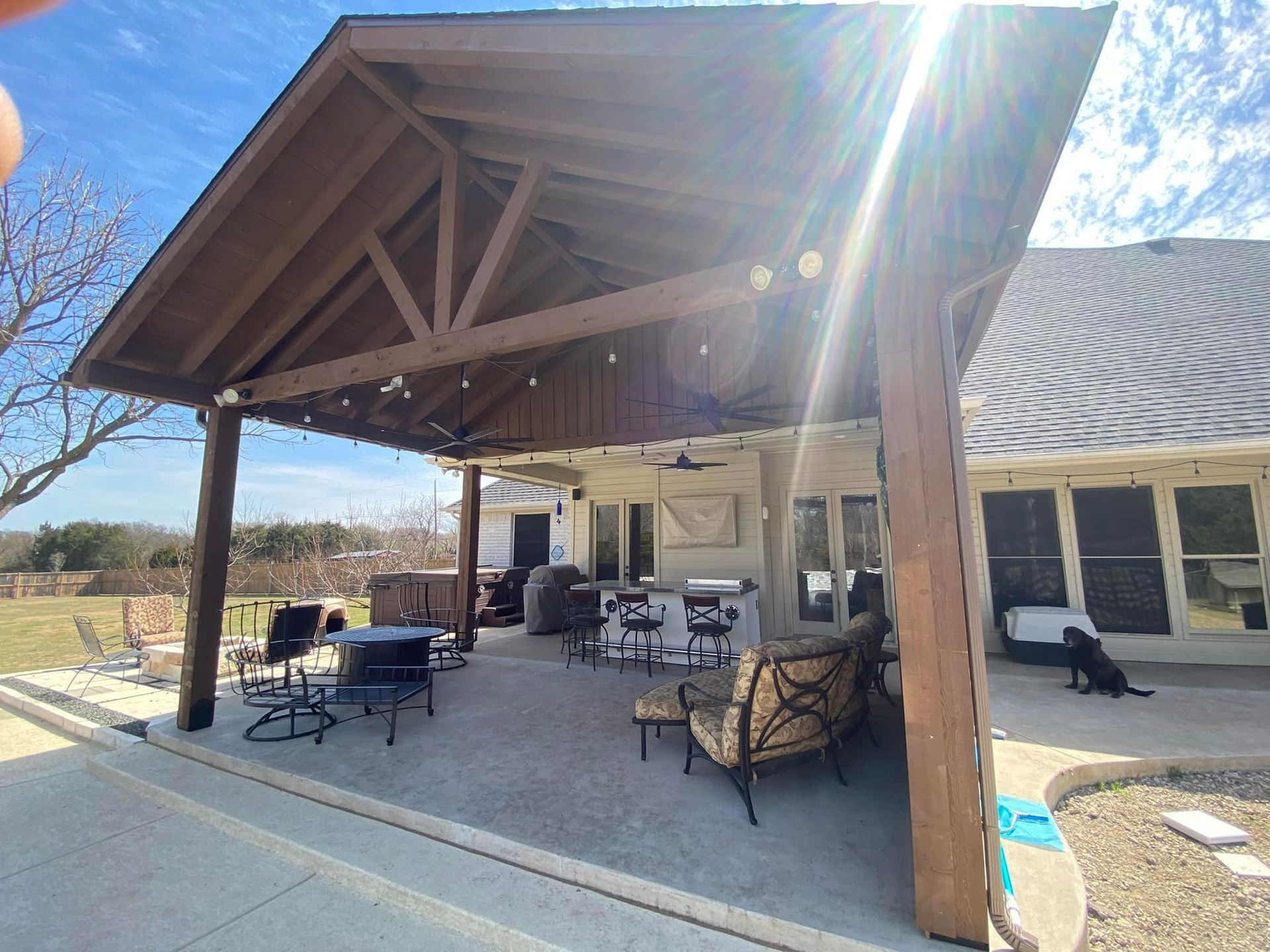 A large covered patio area with a table and chairs under a wooden roof.