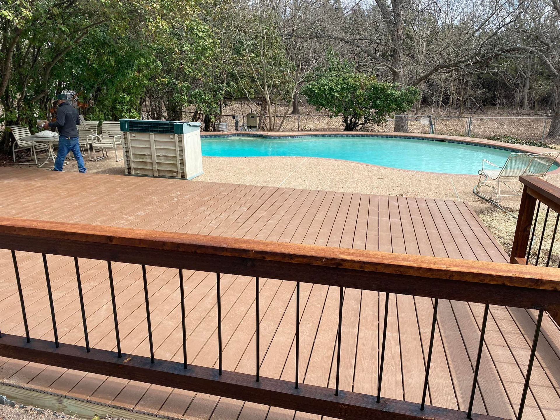 A man is standing on a wooden deck next to a swimming pool.