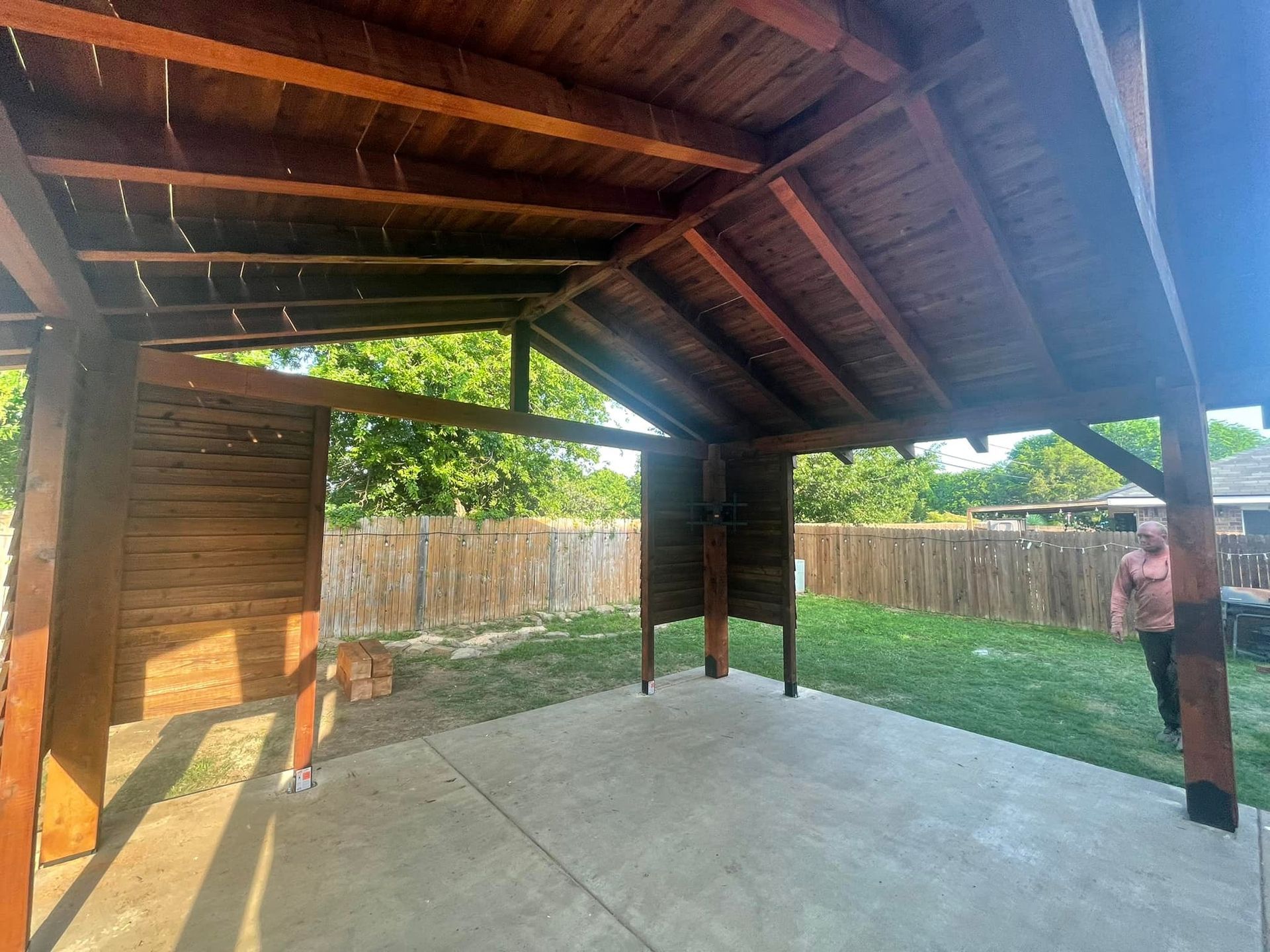 A woman is standing under a wooden pavilion in a backyard.