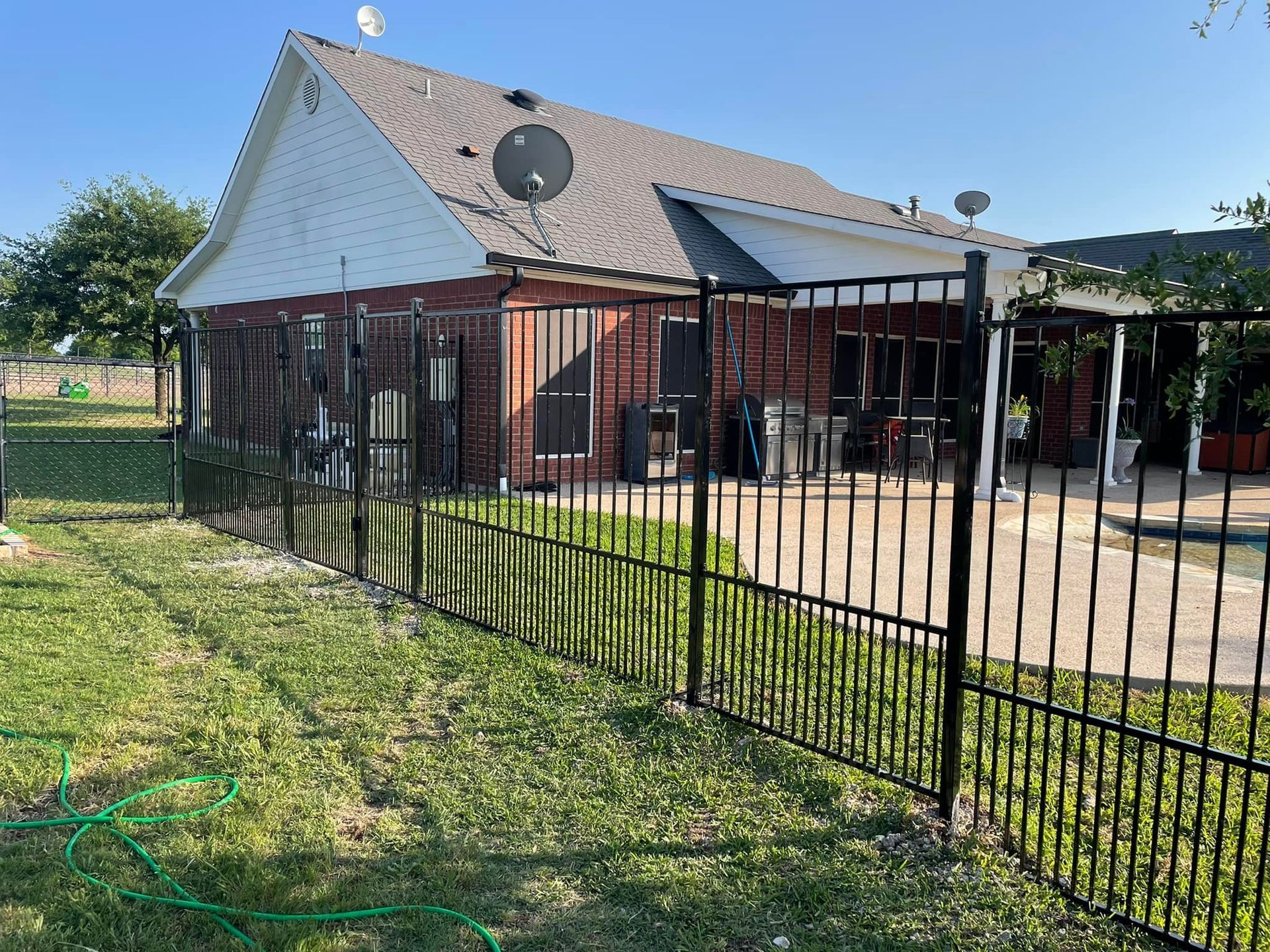 A black fence surrounds a brick house with a satellite dish on the roof.