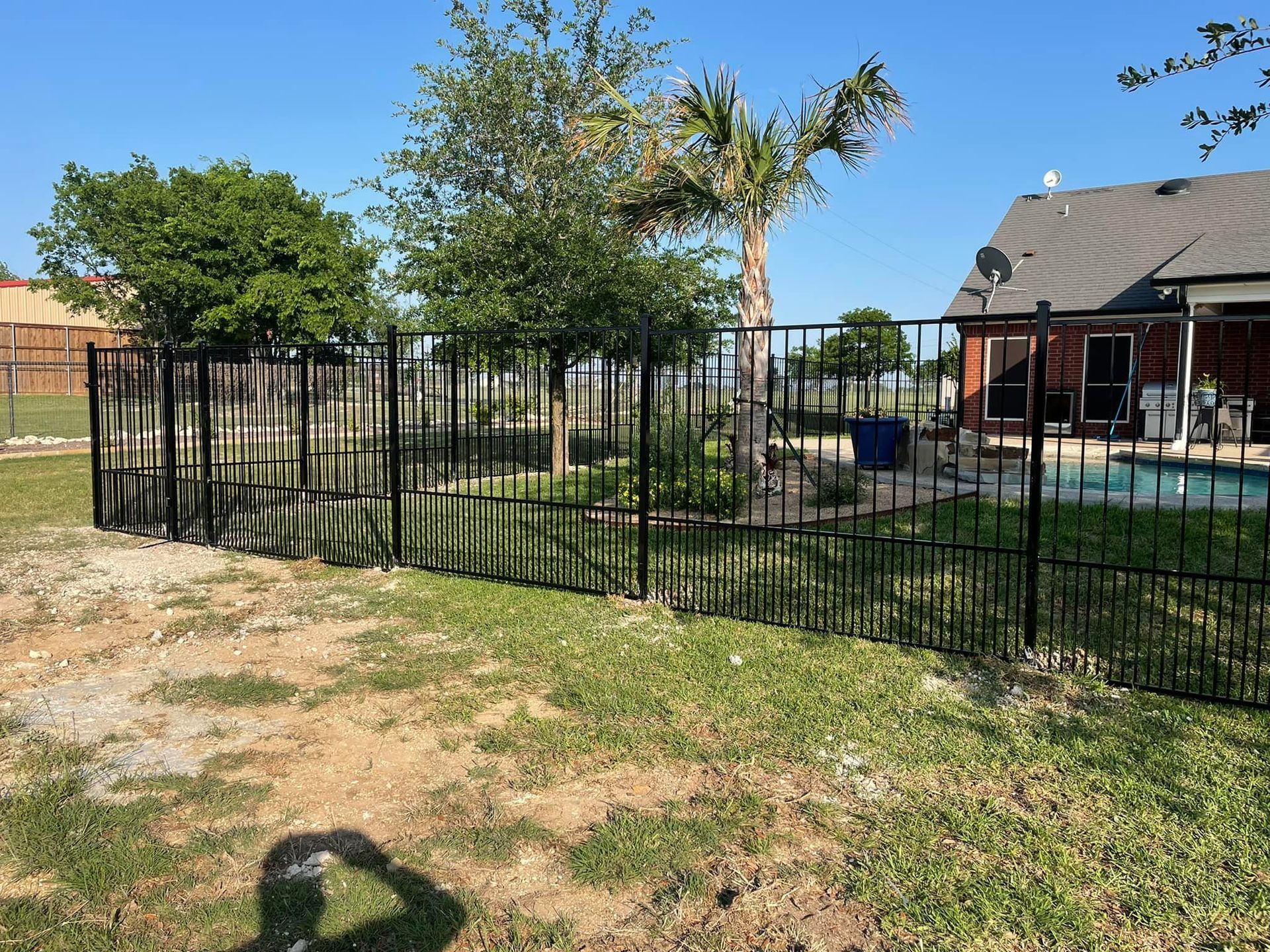 A black metal fence surrounds a swimming pool in a backyard.