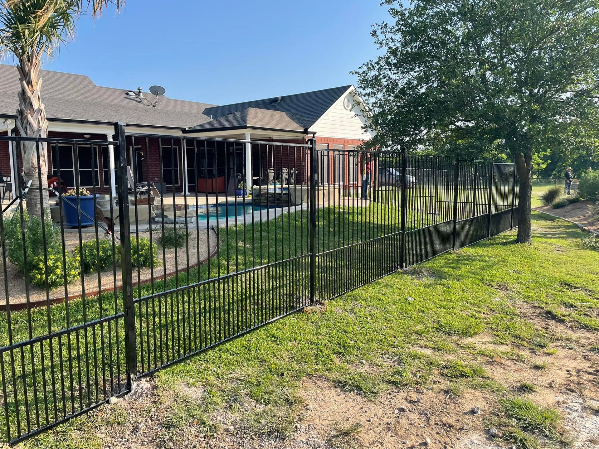 A black metal fence surrounds a lush green yard in front of a house.