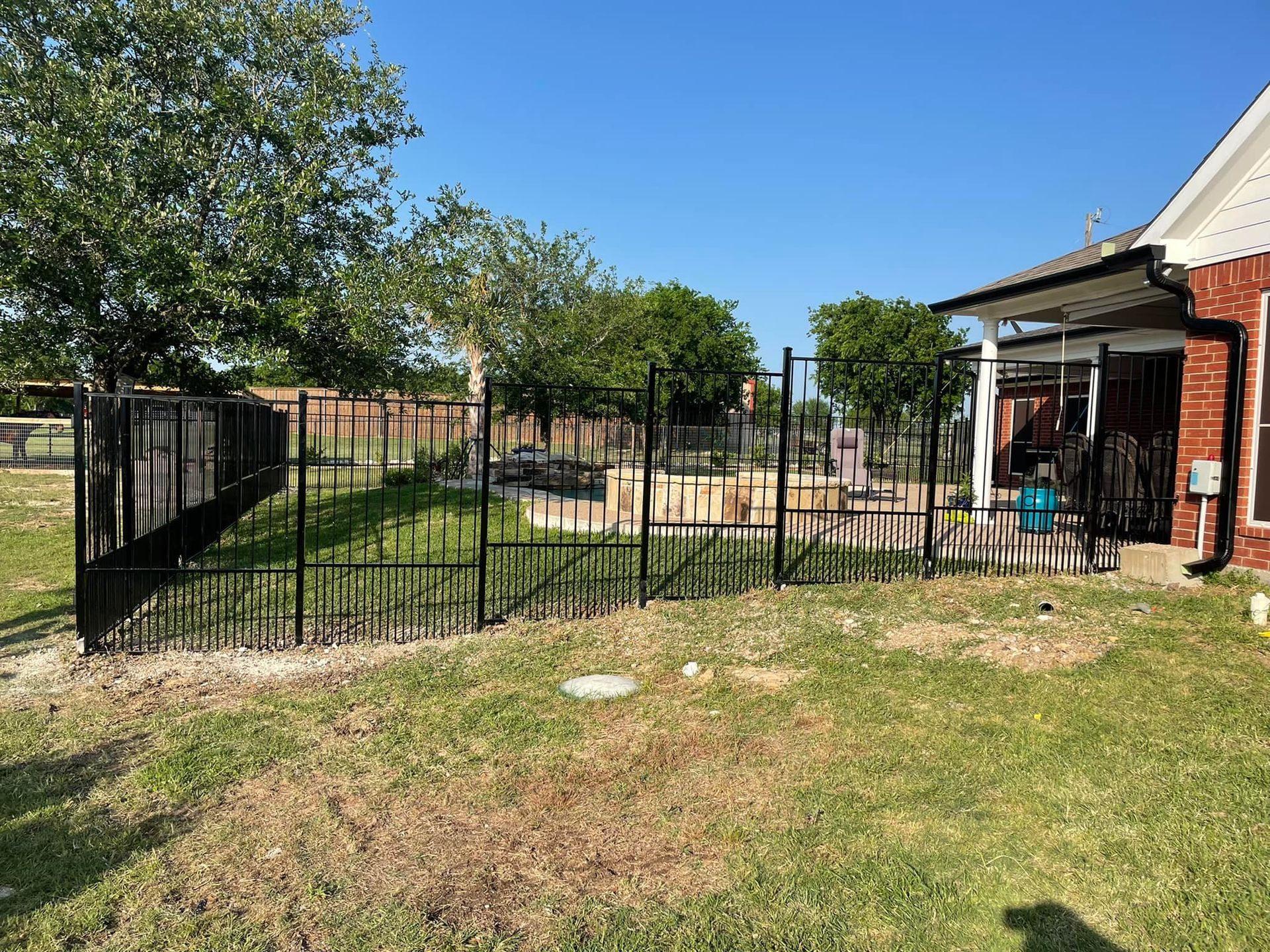 A black metal fence surrounds a lush green yard in front of a brick house.