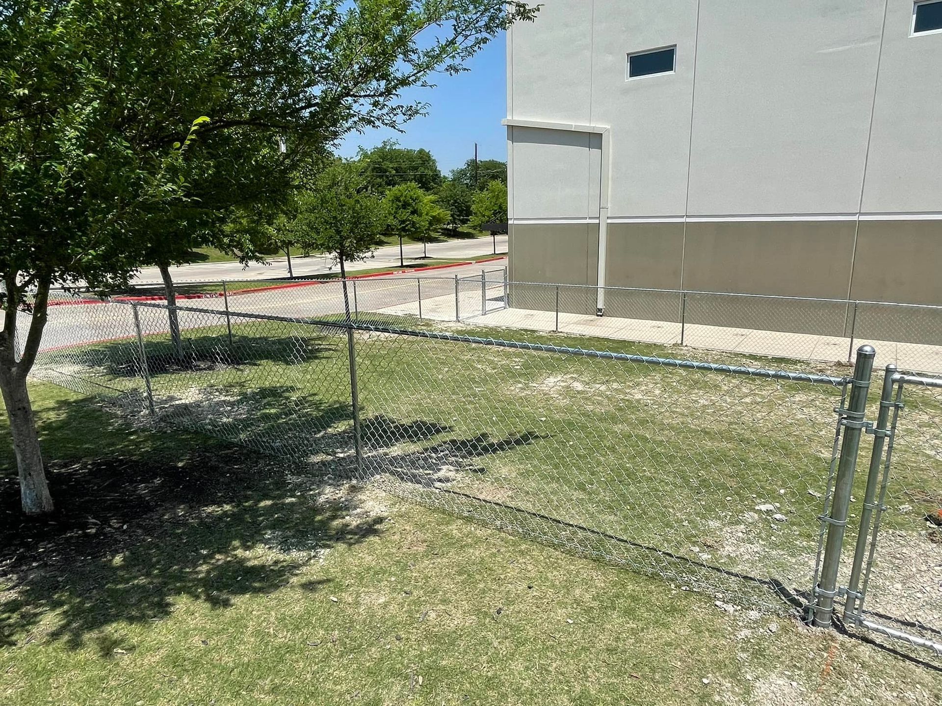 A chain link fence is surrounding a grassy area in front of a building.