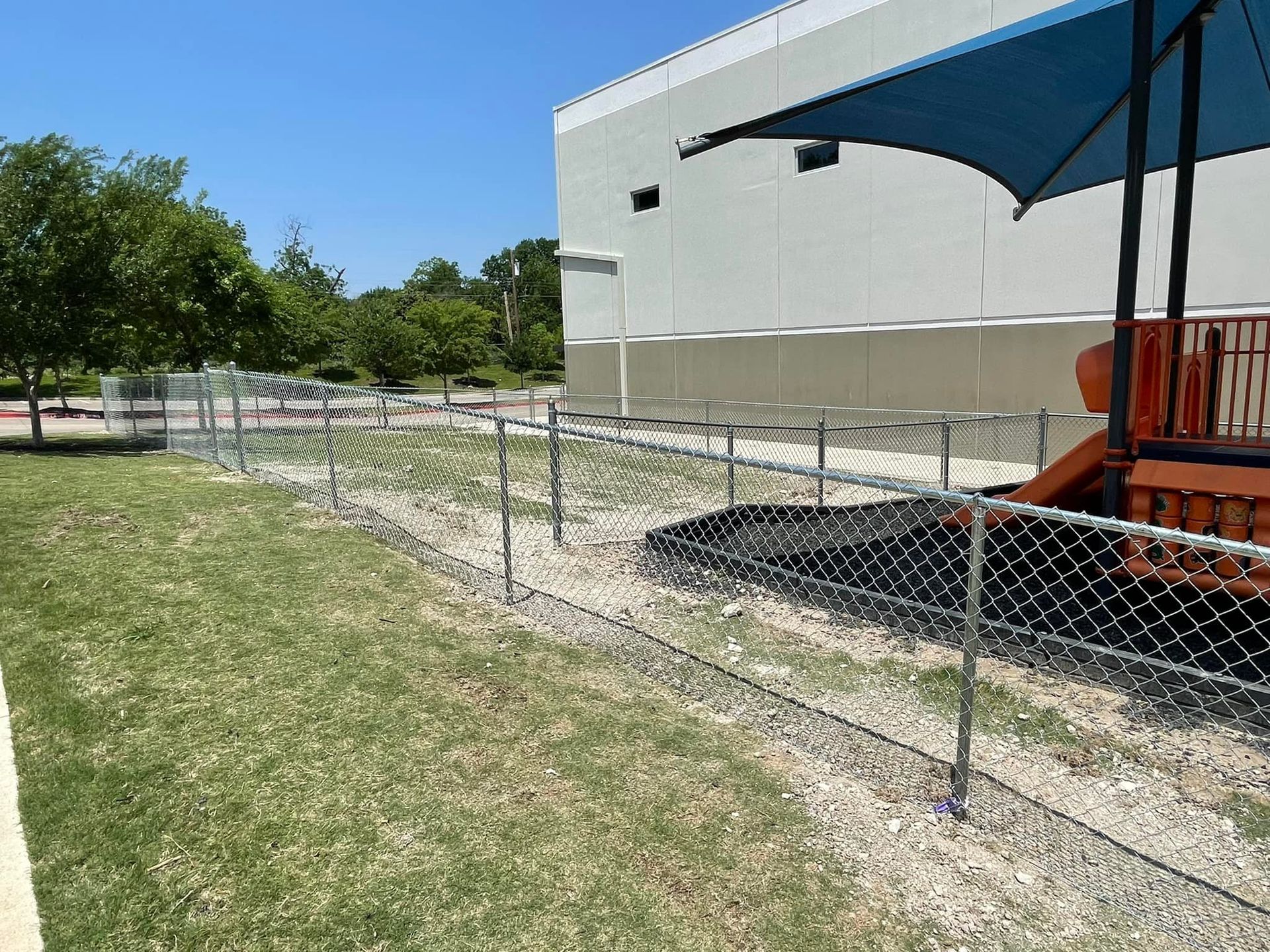A chain link fence surrounds a playground in a park.