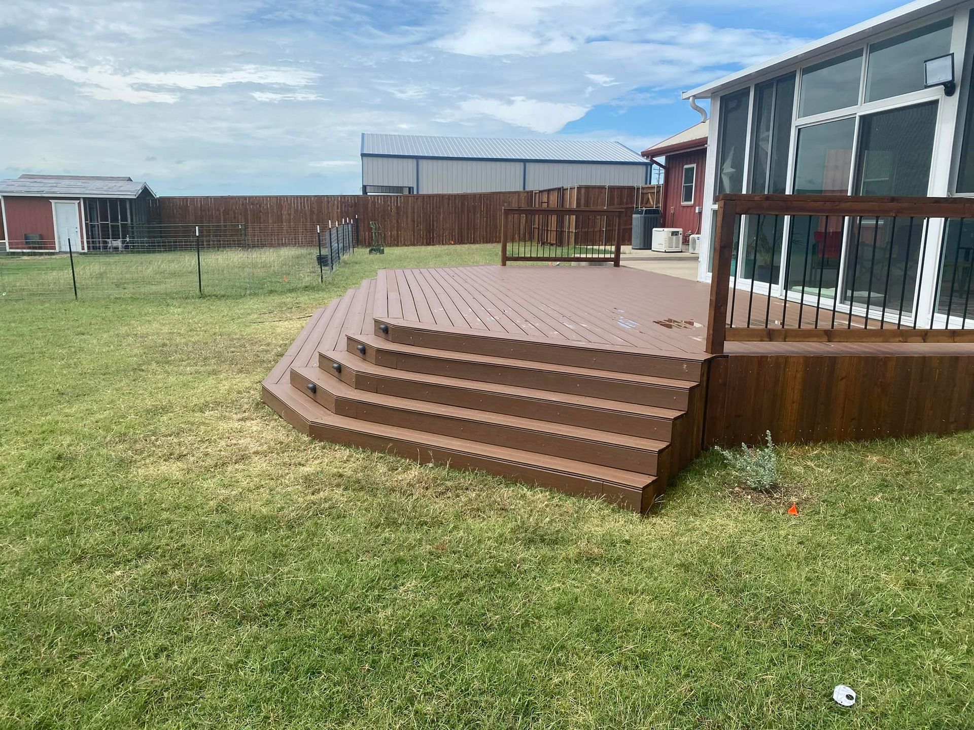 A large deck with stairs leading up to it is in the backyard of a house.