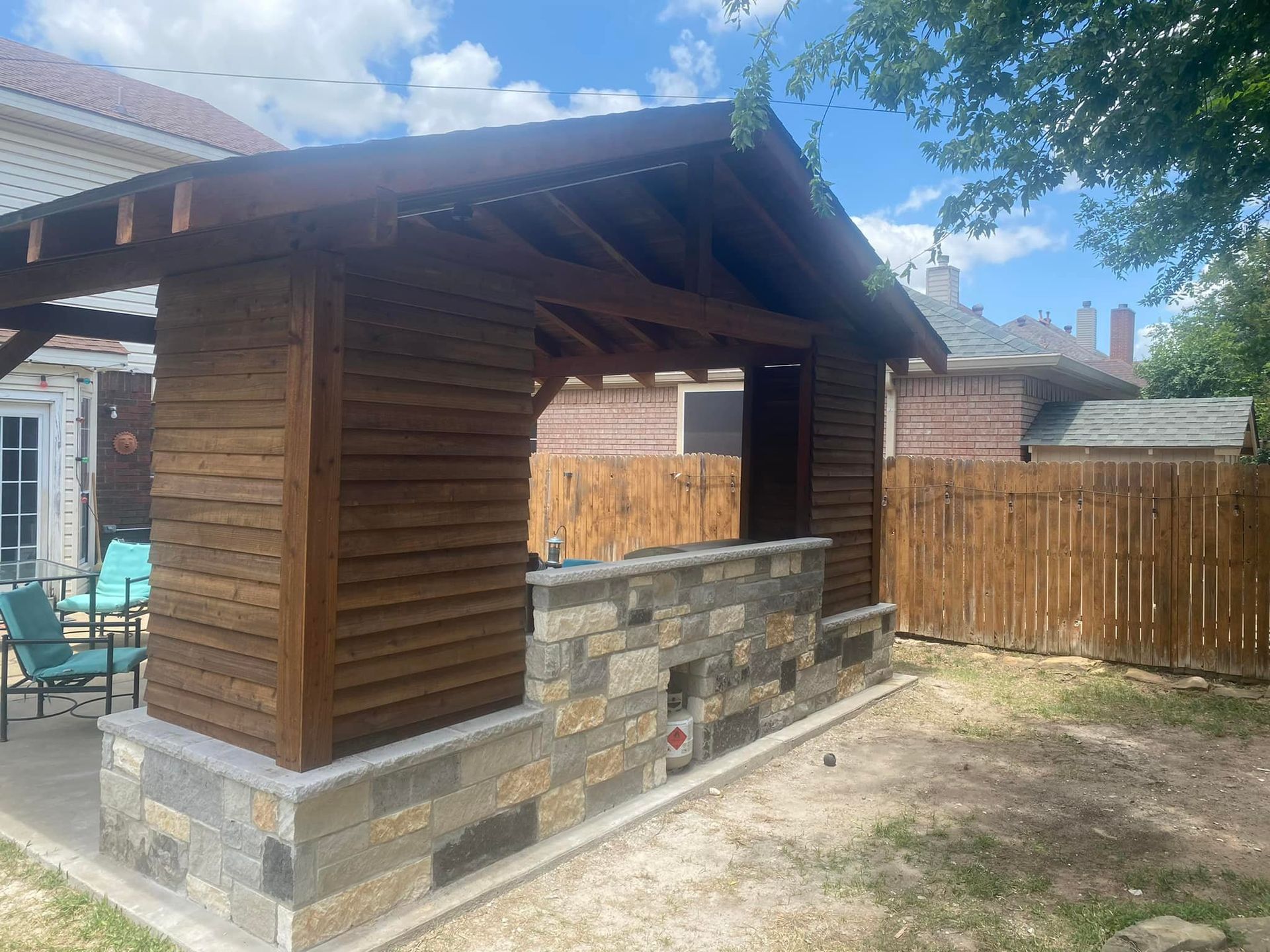 A wooden gazebo with a stone wall in the backyard of a house.