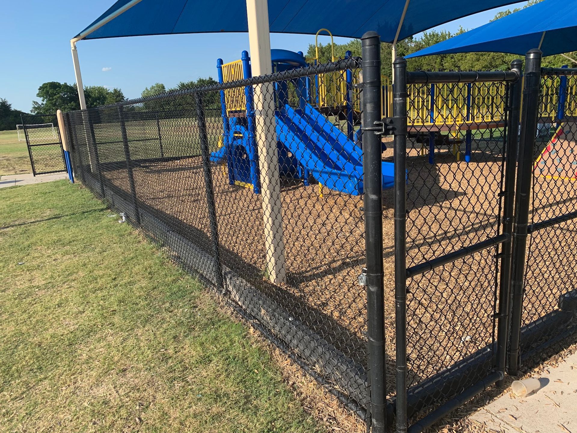A chain link fence surrounds a playground with a blue slide.