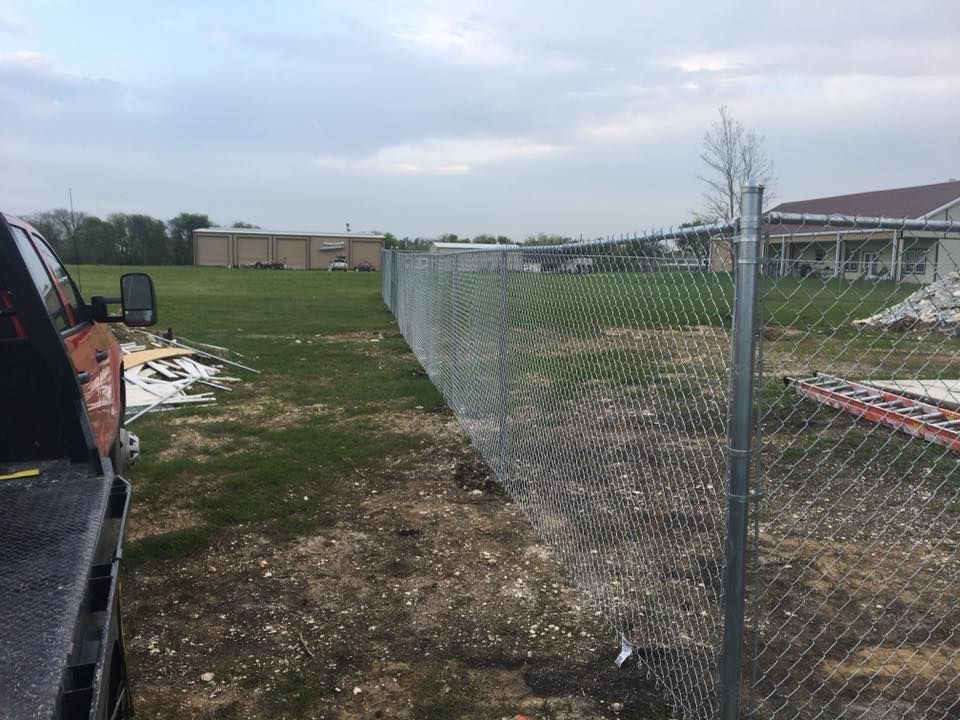 A truck is parked next to a chain link fence in a field.