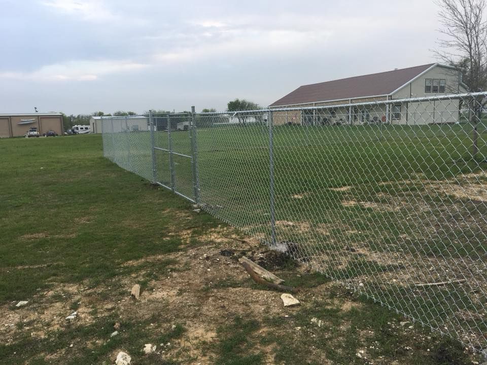 A chain link fence surrounds a grassy field with a house in the background.