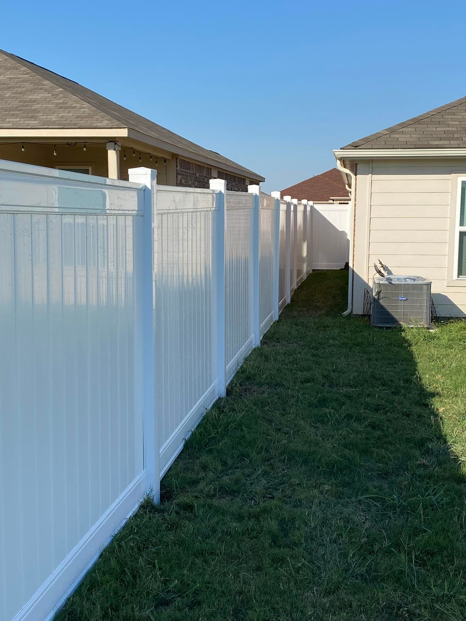 A white fence surrounds a lush green yard next to a house.