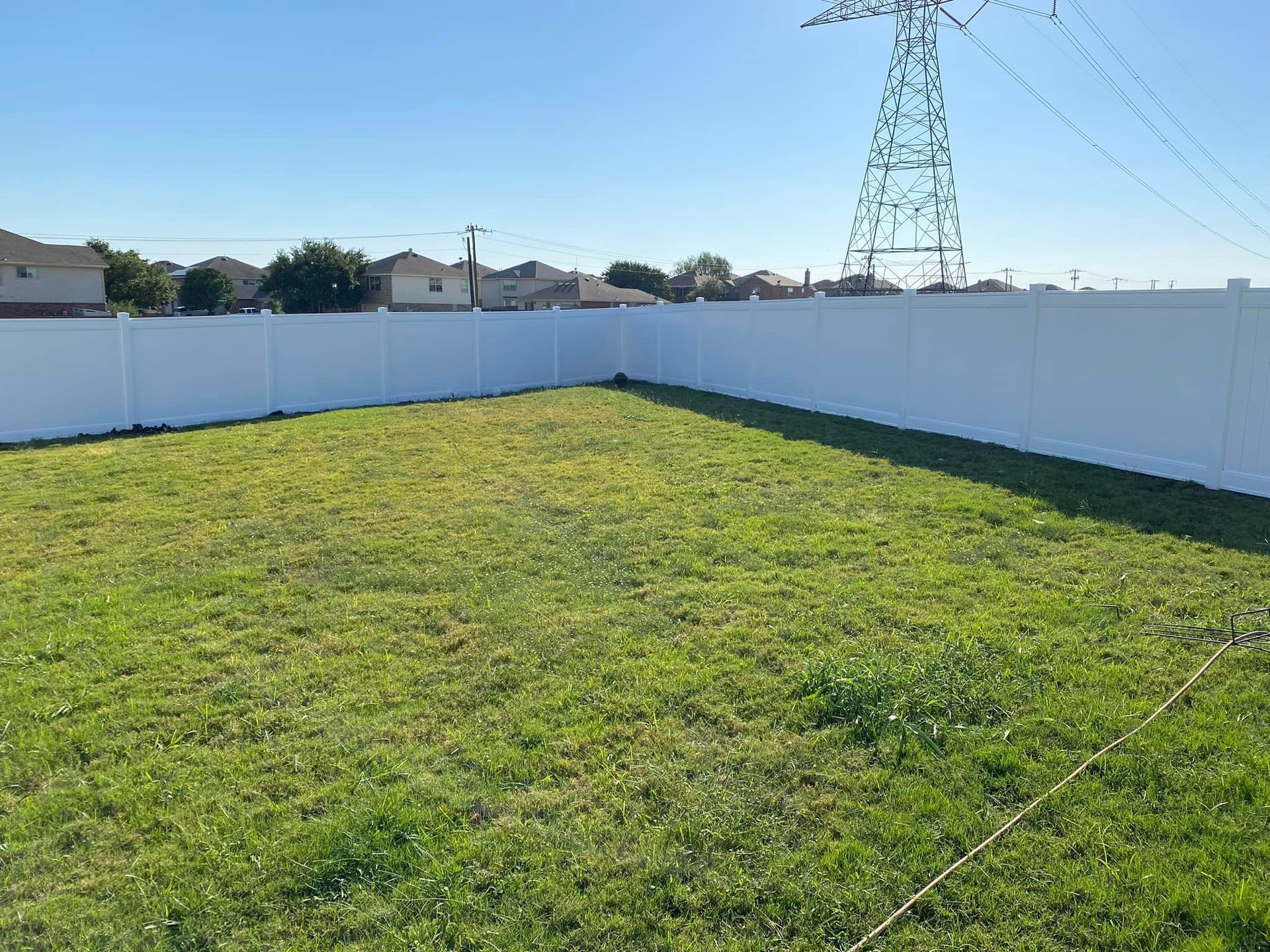 A large lawn with a white fence and a power line in the background.