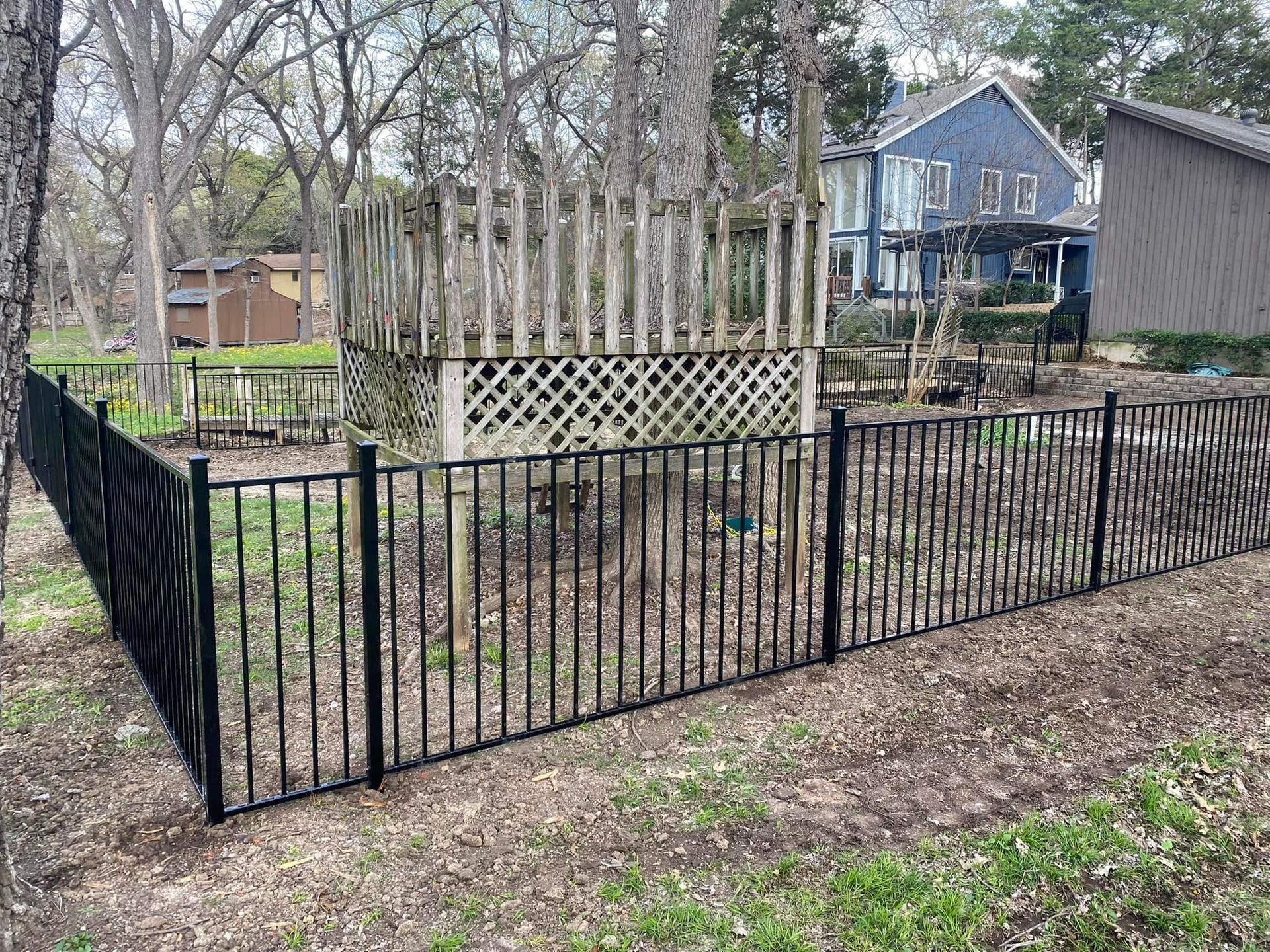A black fence surrounds a yard with a house in the background.