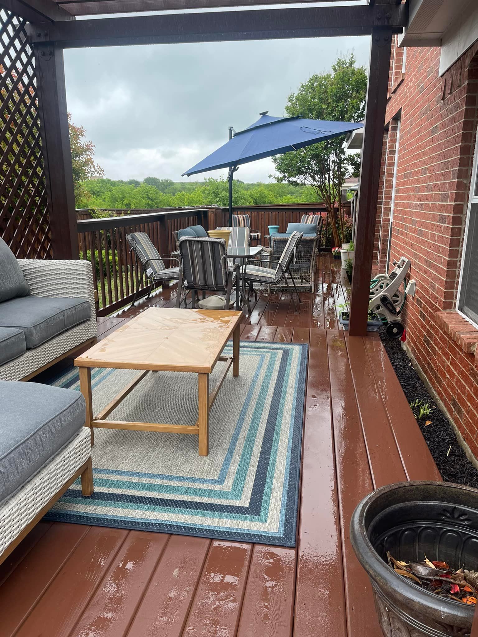 A deck with a couch , table , chairs and umbrella on a rainy day.