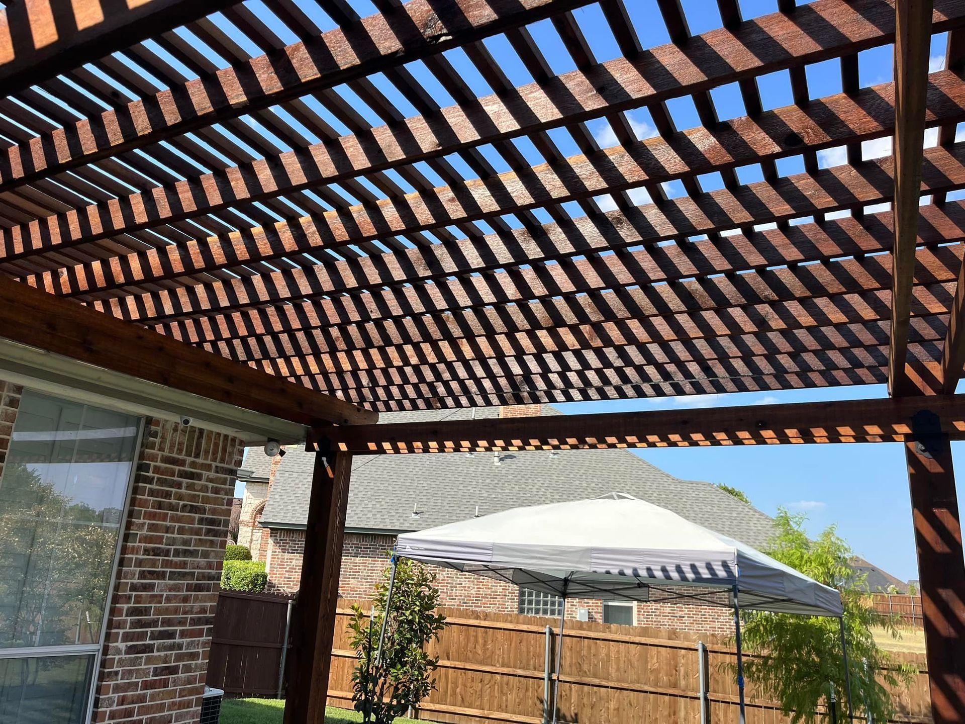 A wooden pergola with a white umbrella in front of a brick house.