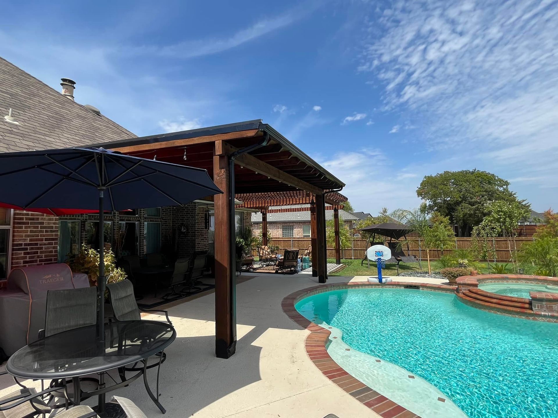A large swimming pool with a table and chairs under a pergola.