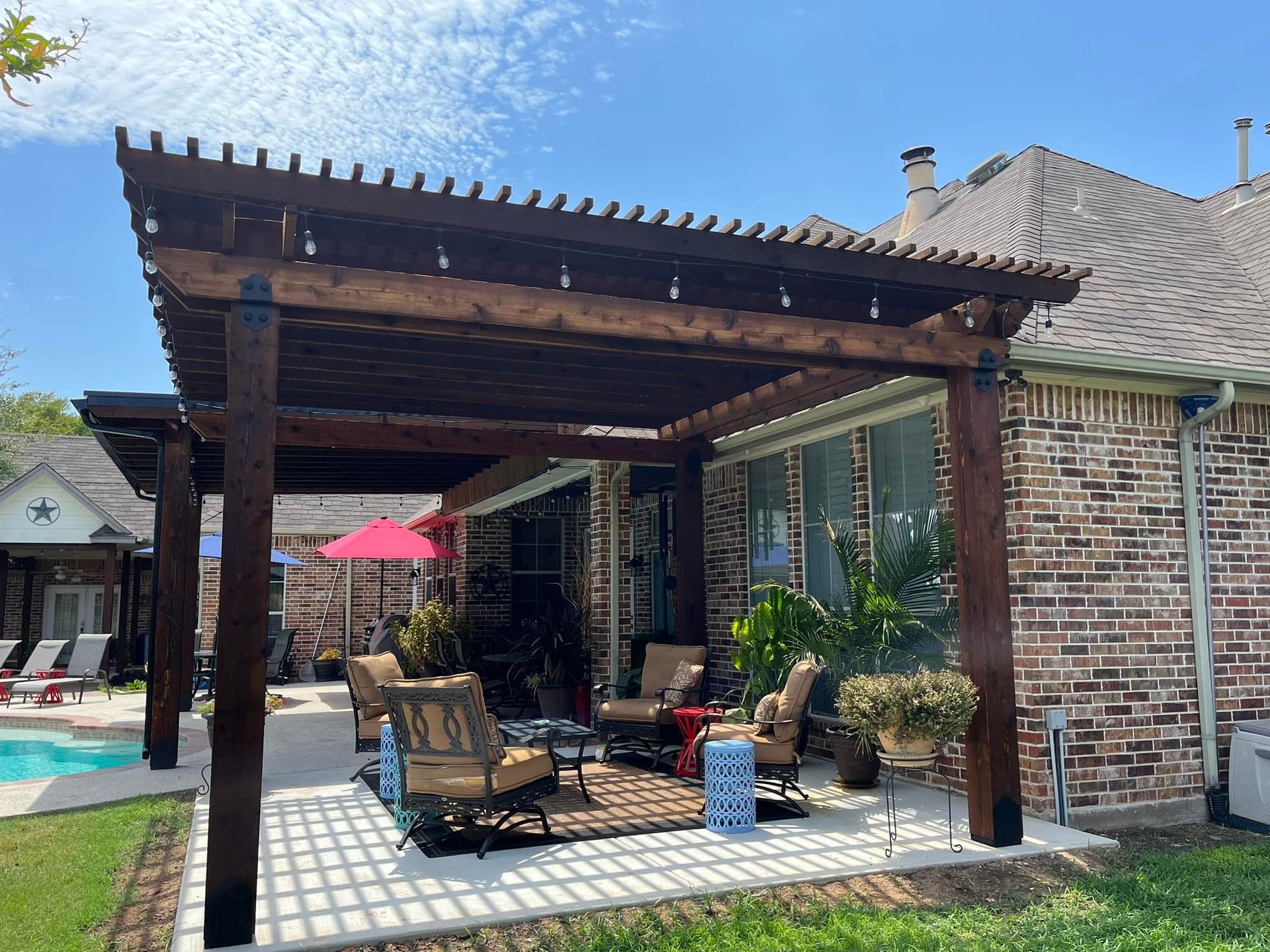 A wooden pergola is sitting in the backyard of a brick house.