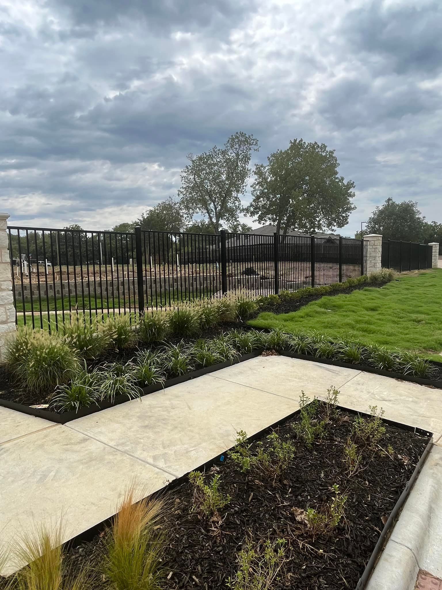 A fence surrounds a lush green field with a walkway leading to it.