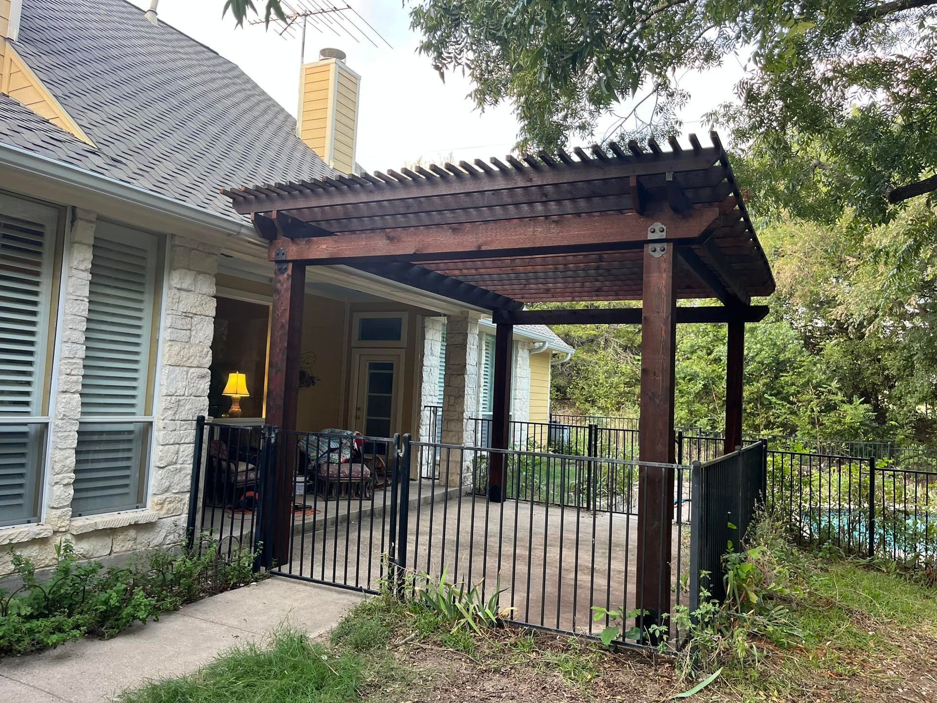 A wooden pergola is attached to the side of a house.