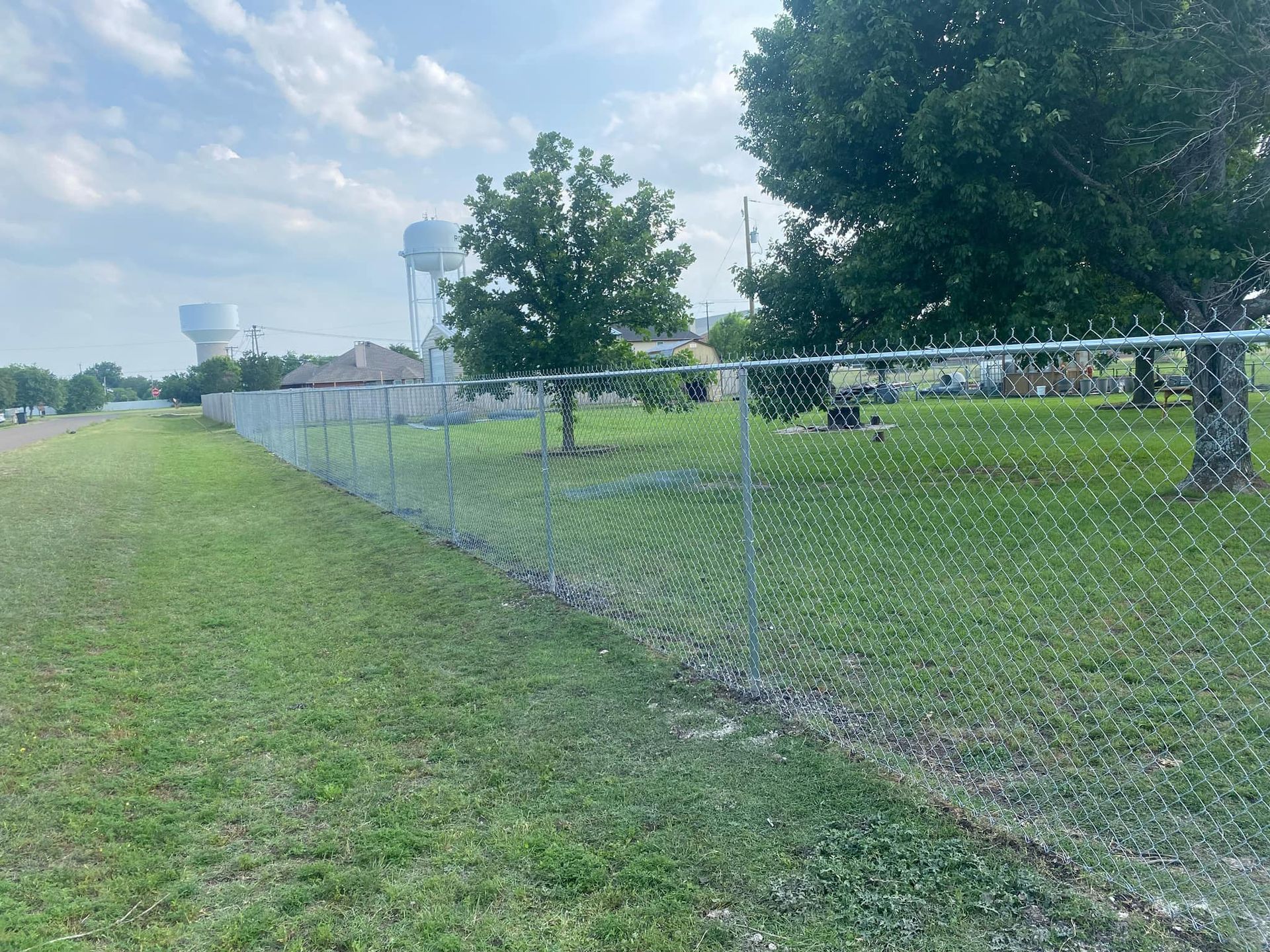 A chain link fence surrounds a grassy field with trees and a water tower in the background.