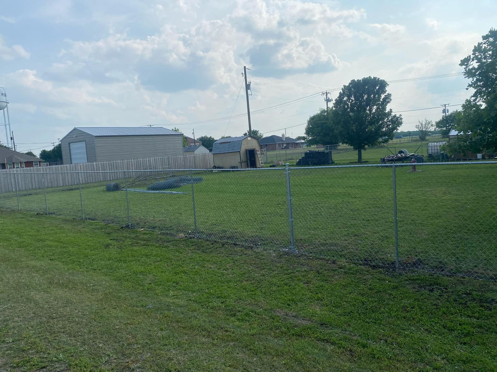 A fence surrounds a grassy field with a building in the background.
