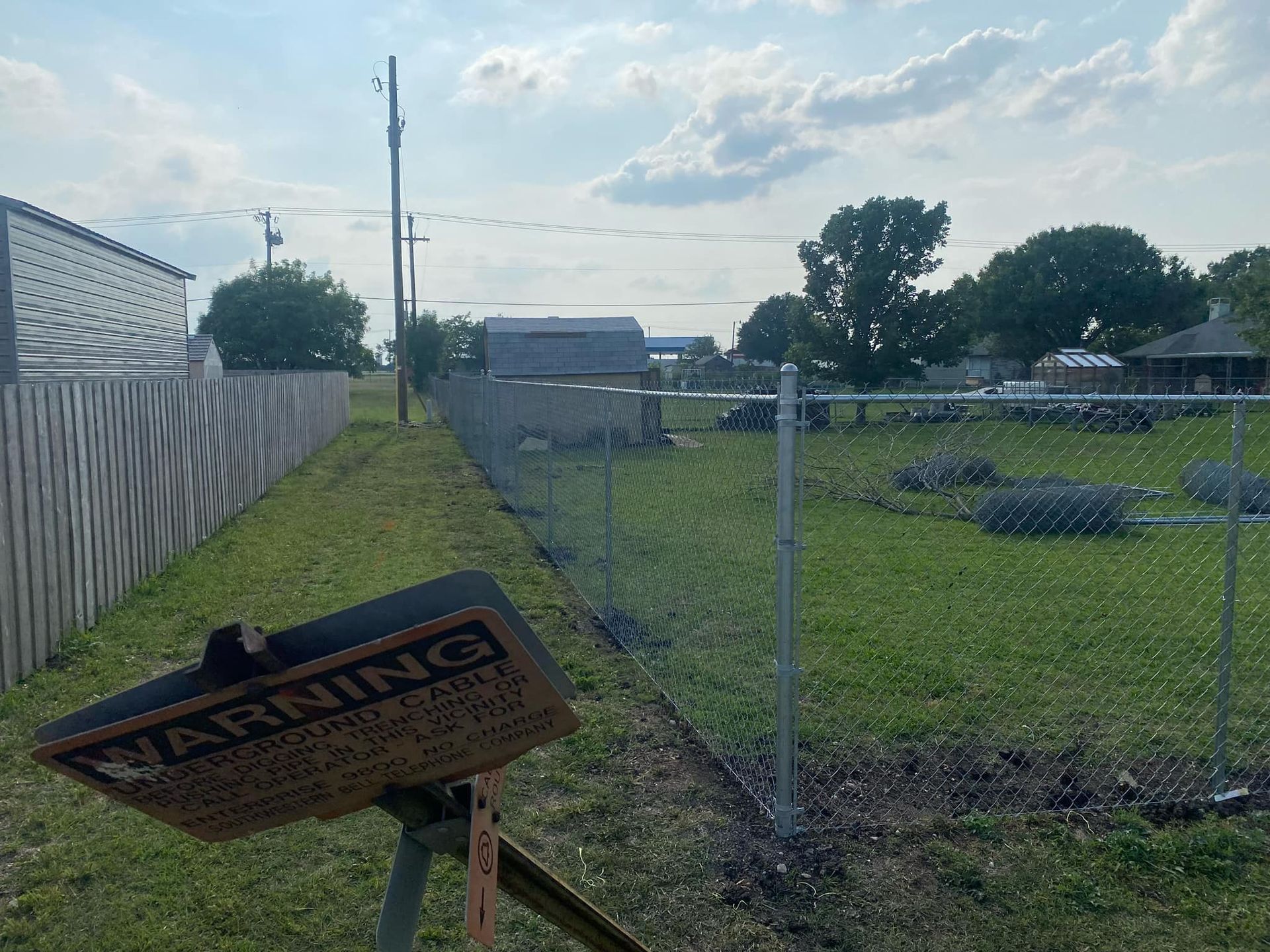 A warning sign is sitting next to a chain link fence.