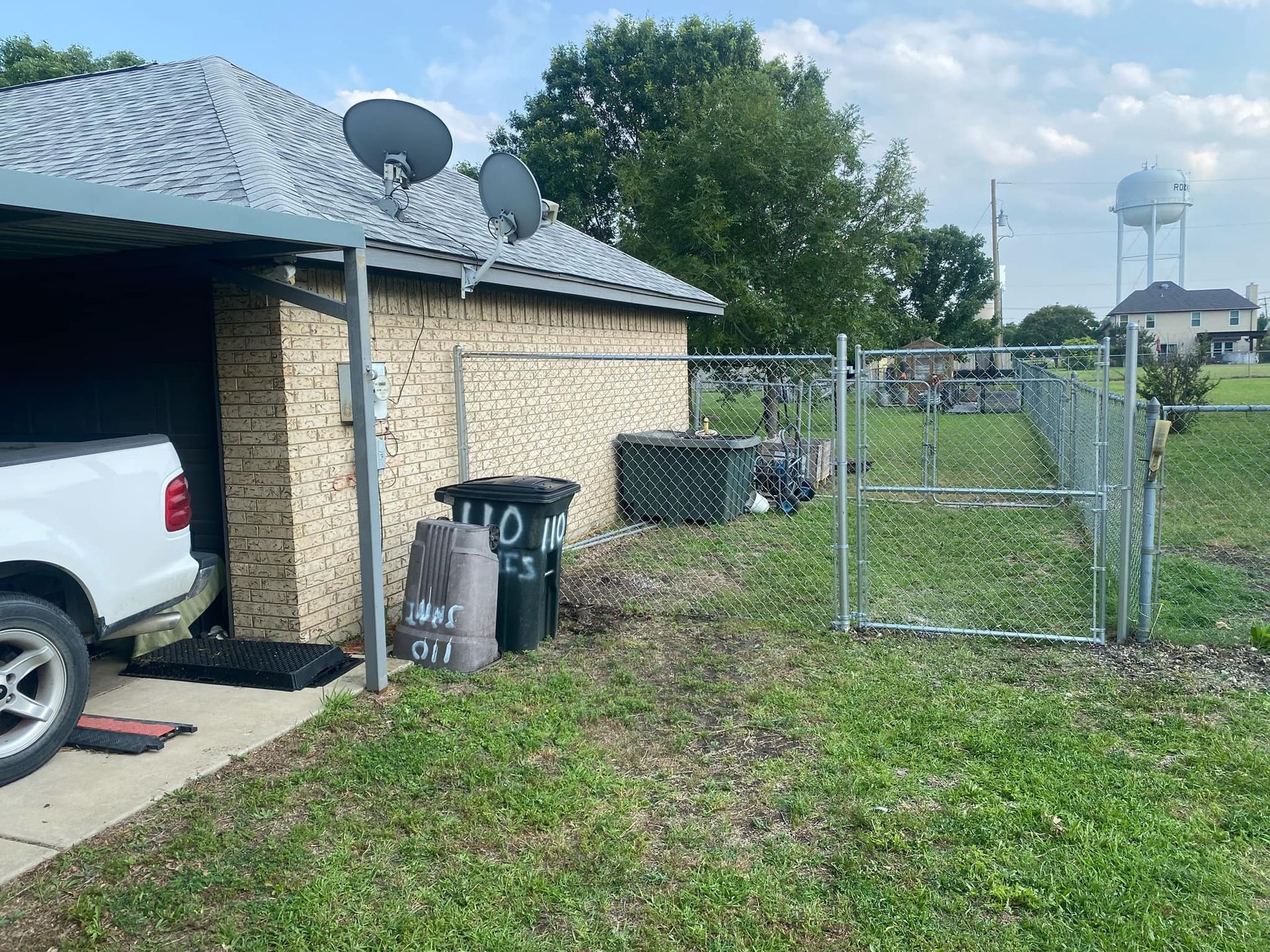 A white truck is parked in front of a house next to a fence.