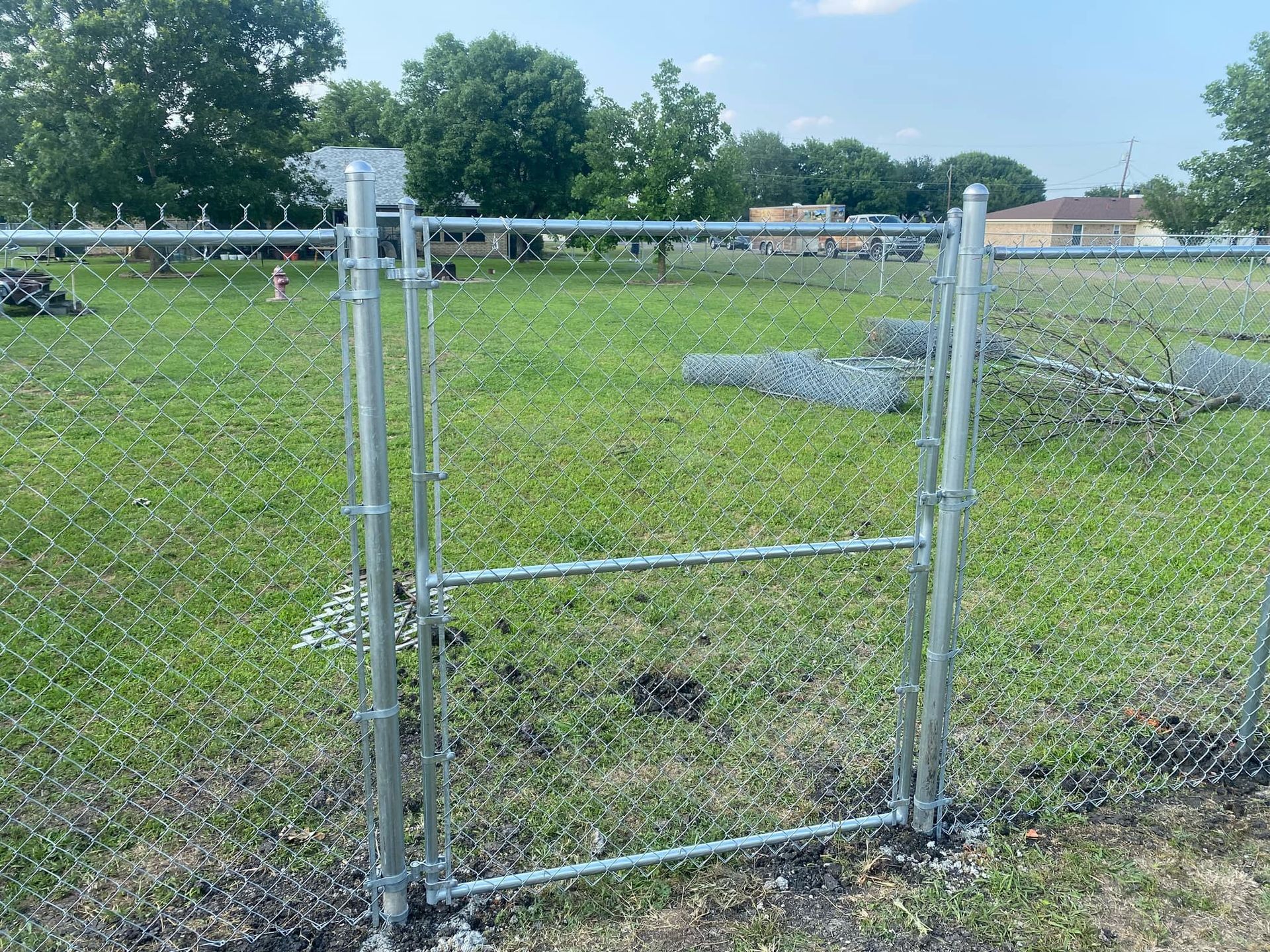 A chain link fence with a gate in the middle of a grassy field.