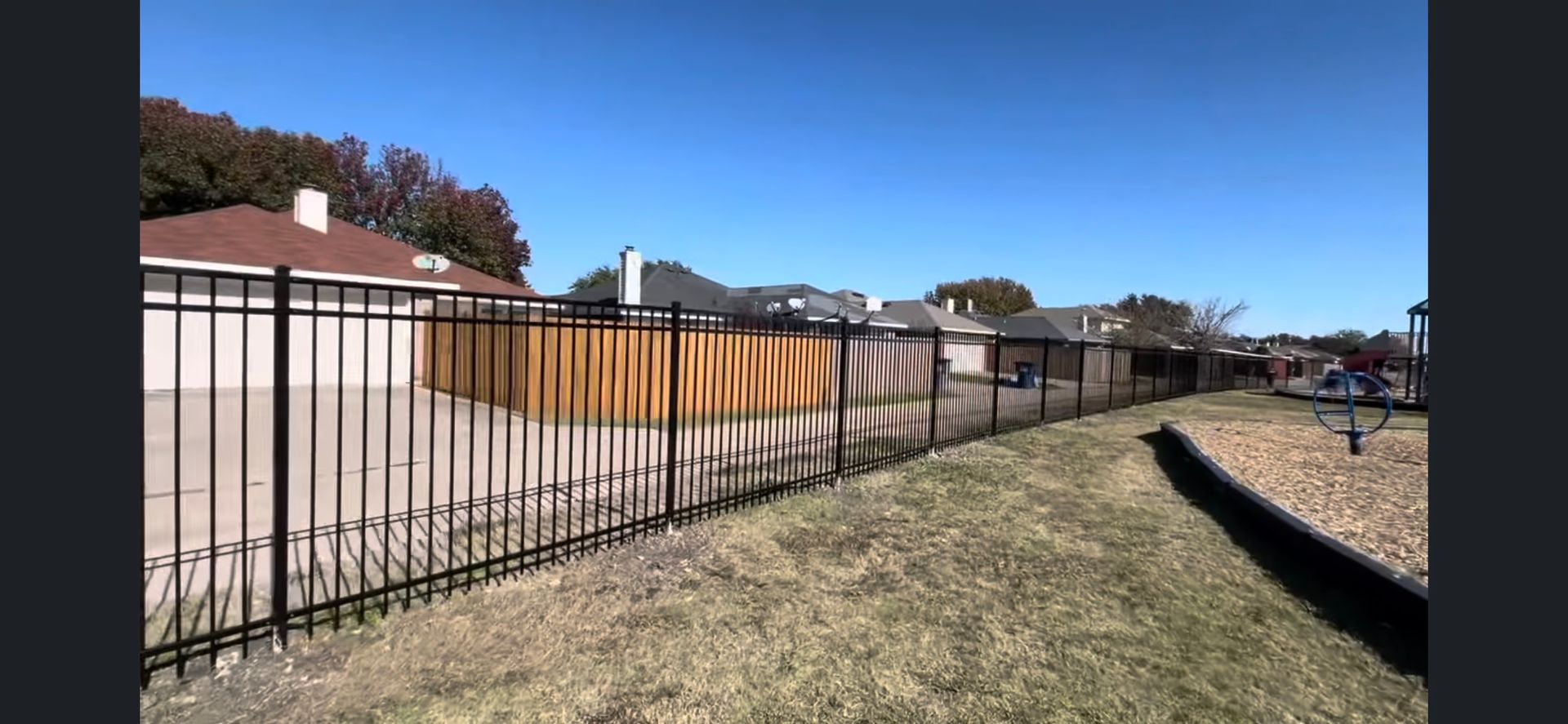 A black metal fence surrounds a yard with a playground in the background.