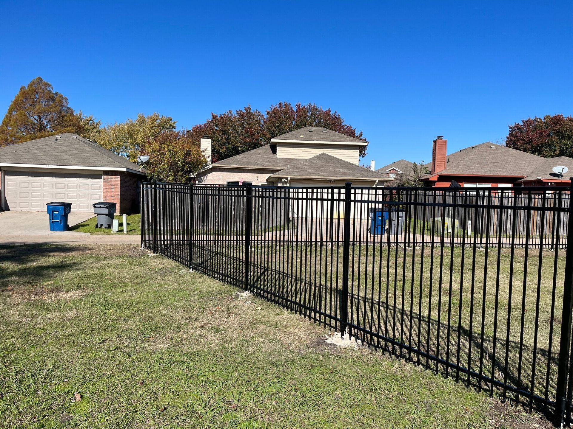 A black fence surrounds a grassy yard in front of a house.