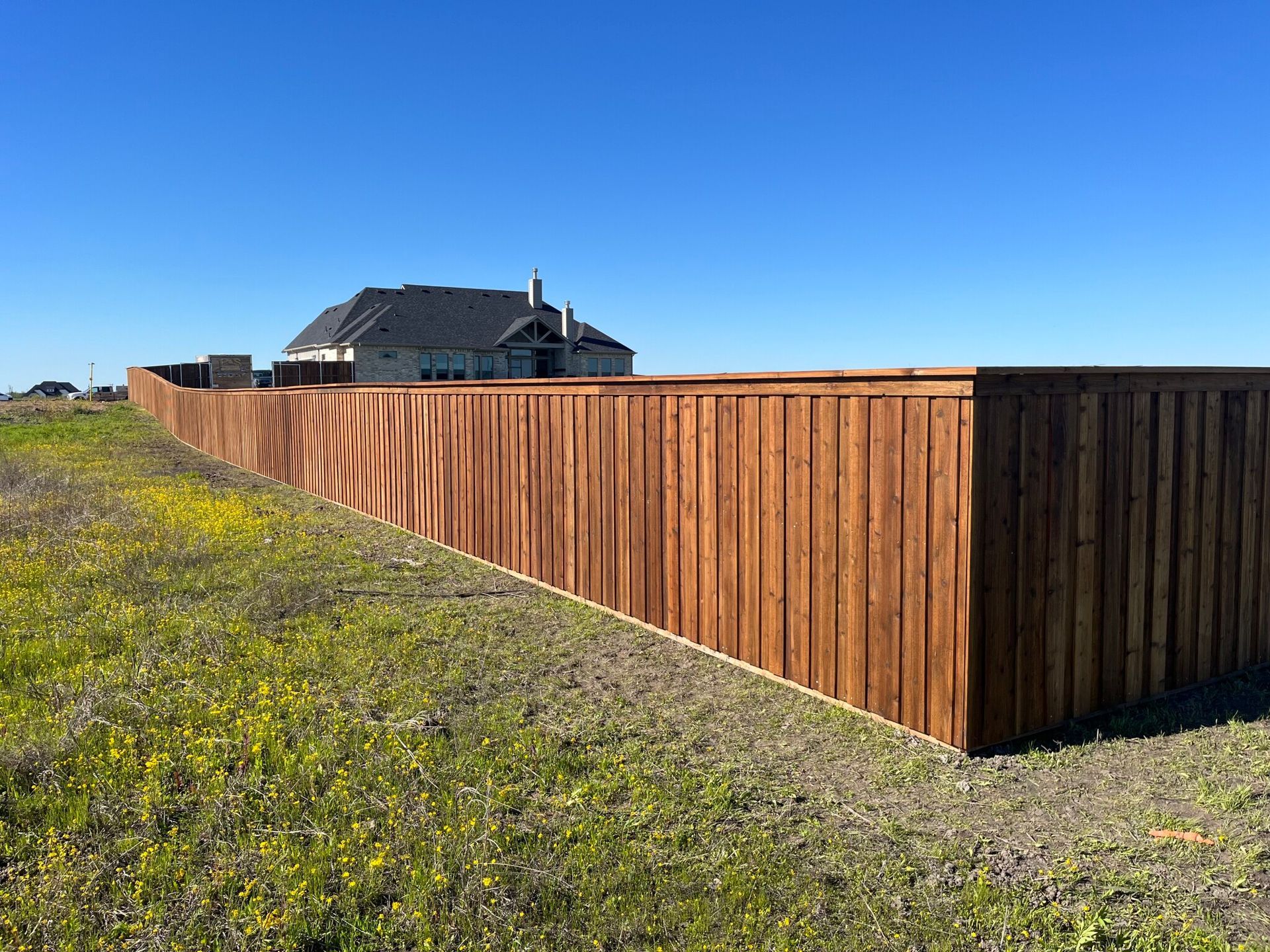 A wooden fence surrounds a grassy field with a house in the background.