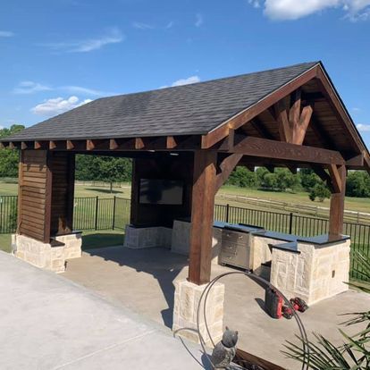 A wooden pavilion with a roof and a fence in the background.