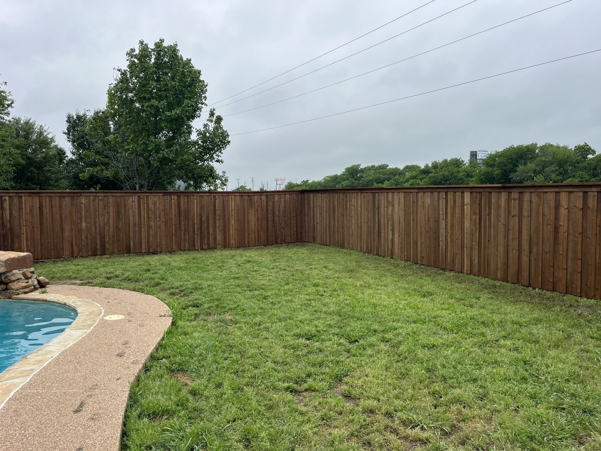 A wooden fence surrounds a swimming pool in a backyard.