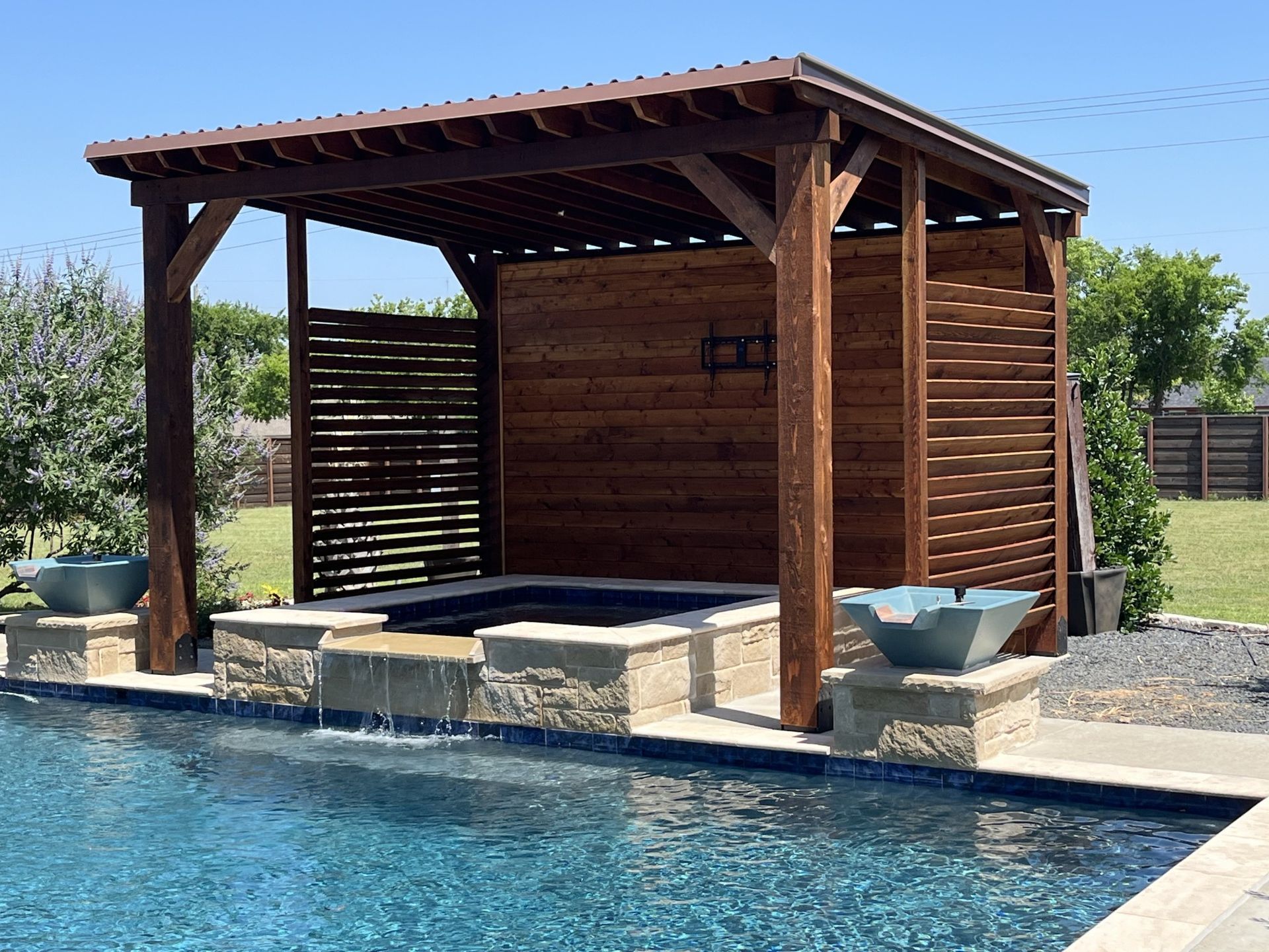 A wooden pergola over a swimming pool with a waterfall.