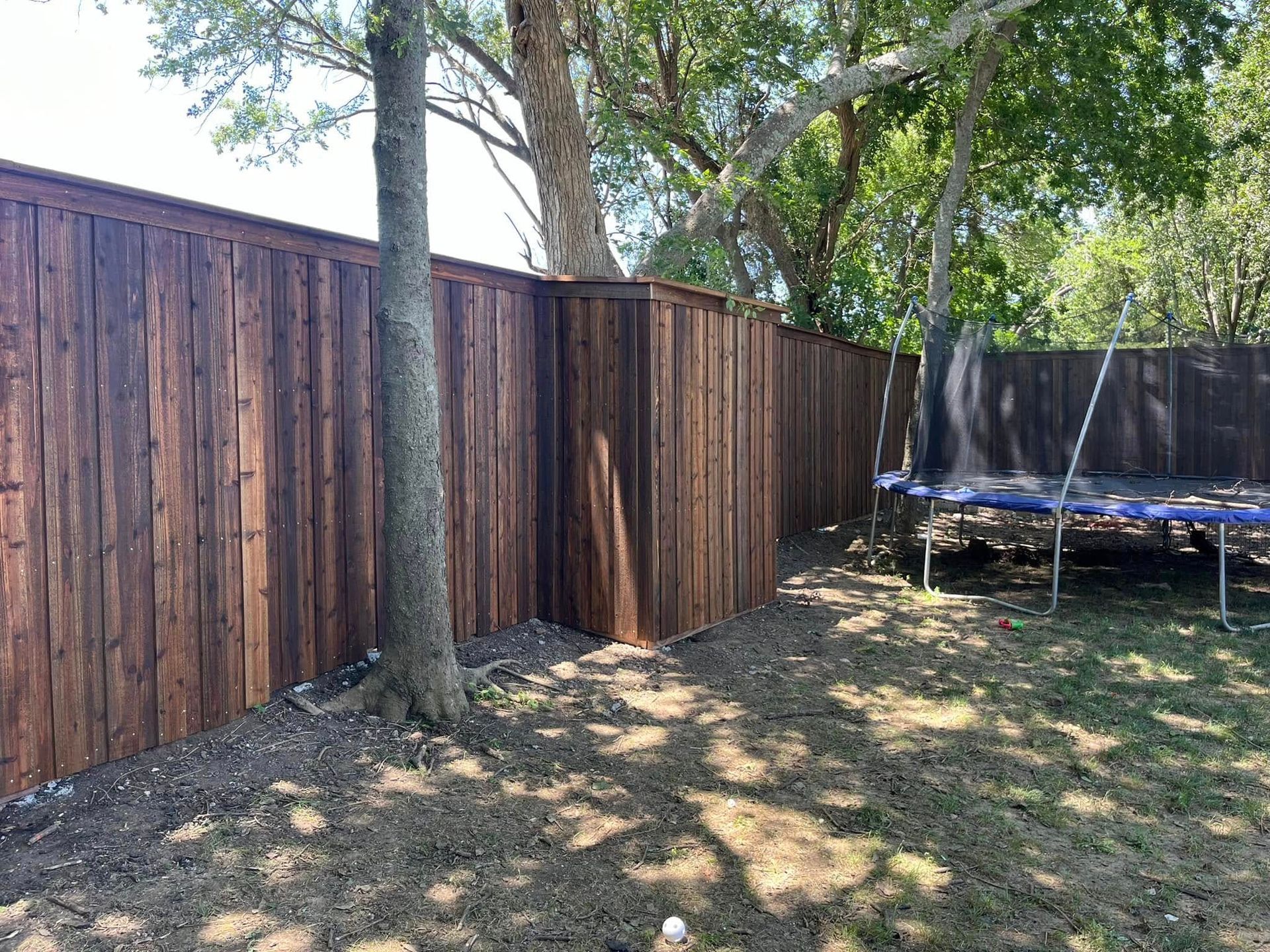 There is a trampoline in the backyard next to a wooden fence.