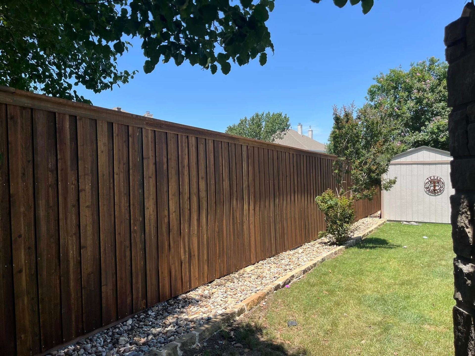 A wooden fence surrounds a lush green yard in a backyard.