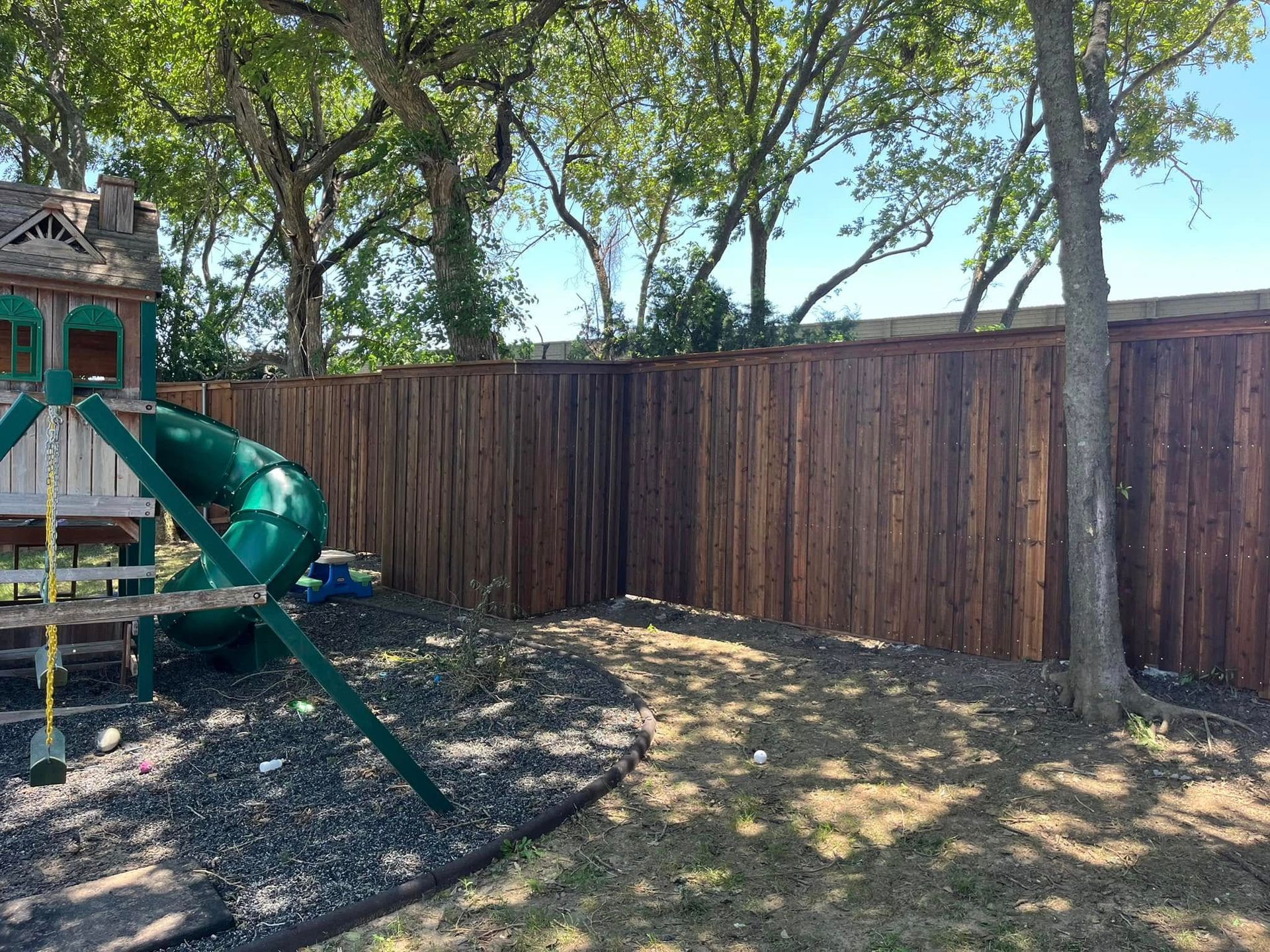 A wooden fence surrounds a playground in a backyard.