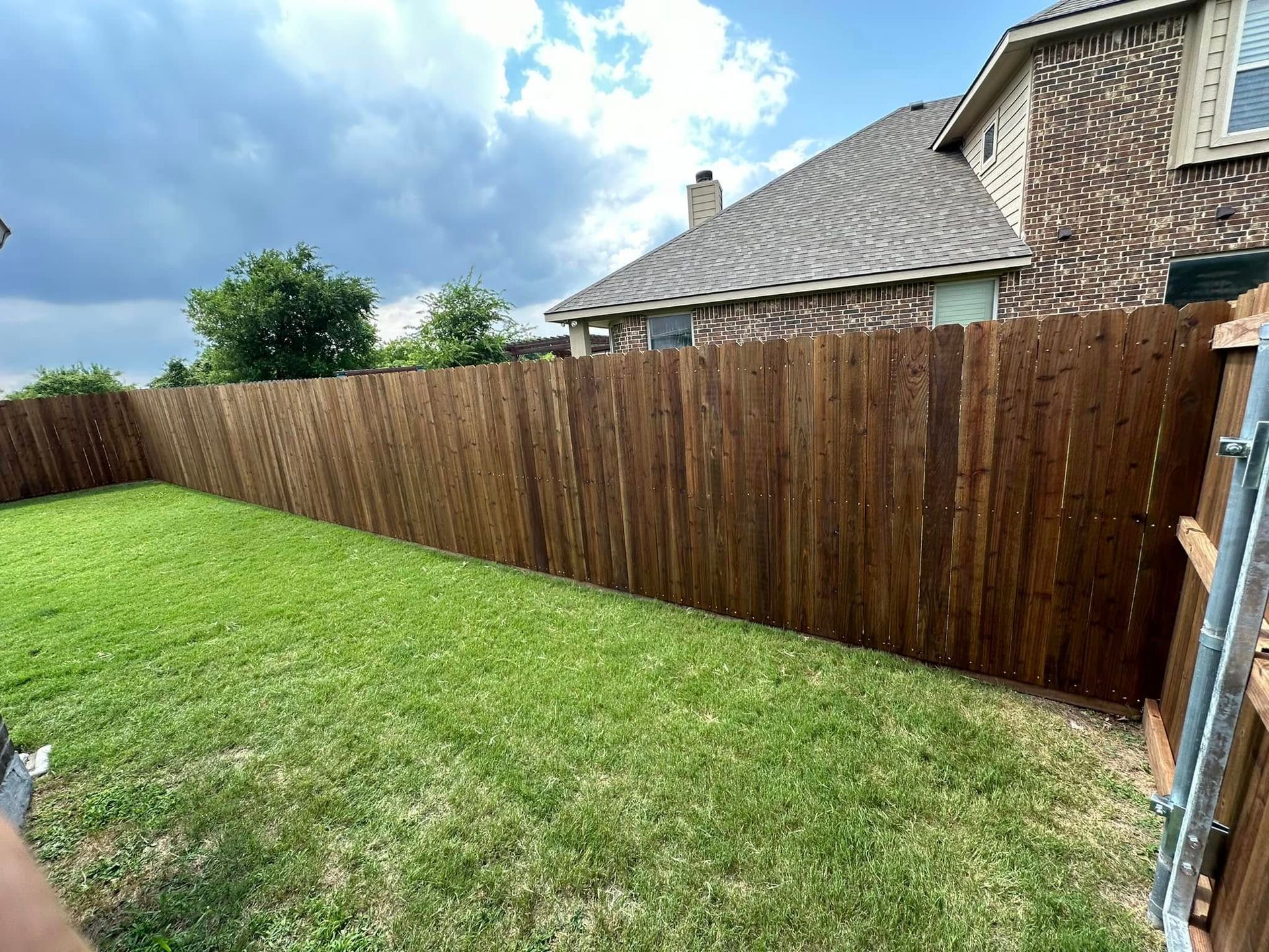 A wooden fence surrounds a lush green yard in front of a house.