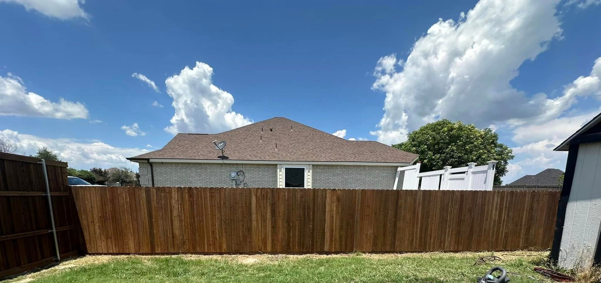 A backyard with a wooden fence and a house in the background.