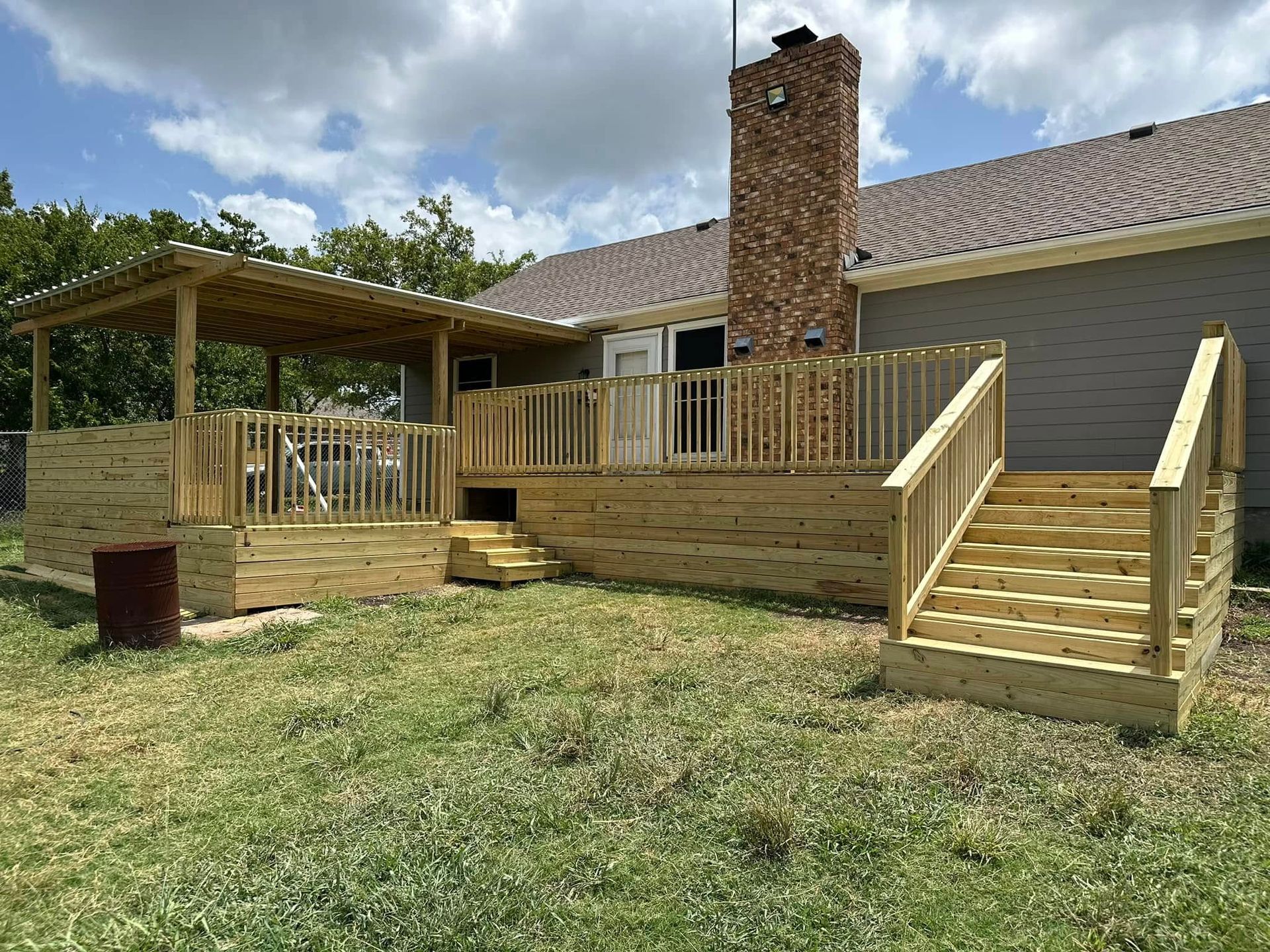 A large wooden deck with stairs and a pergola in the backyard of a house.