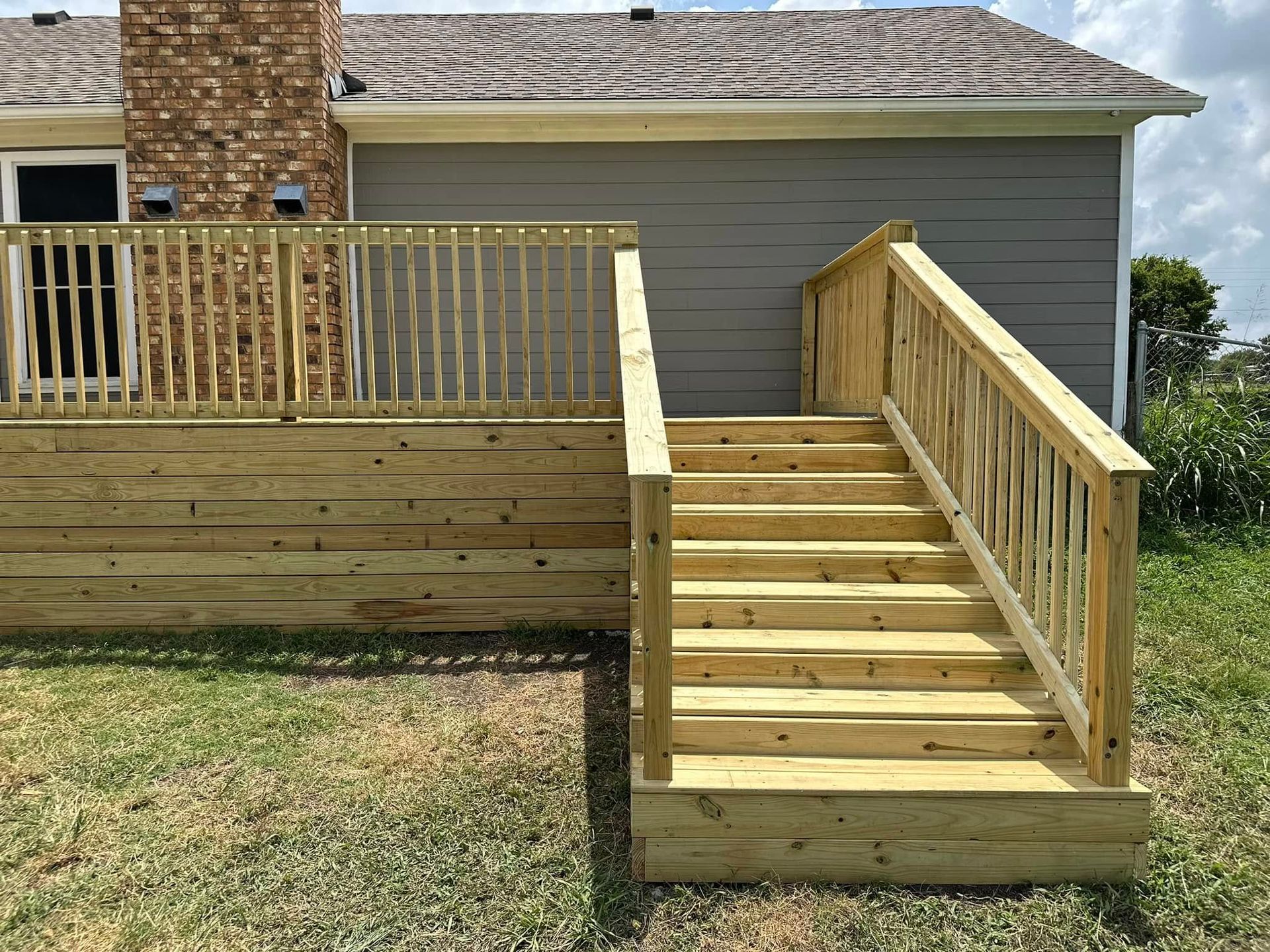 A wooden deck with stairs leading up to it is in front of a house.