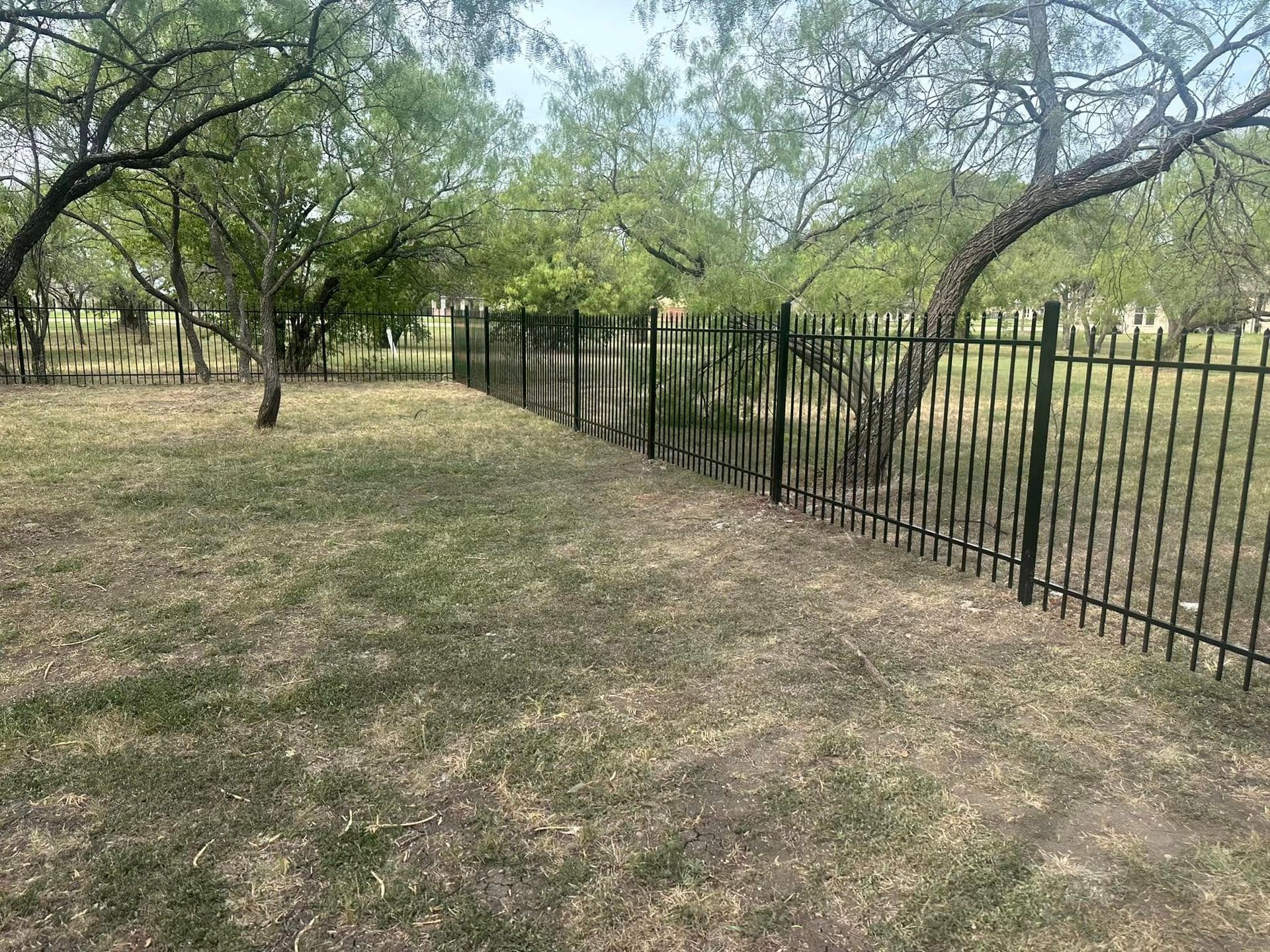 A metal fence surrounds a grassy field in a park.
